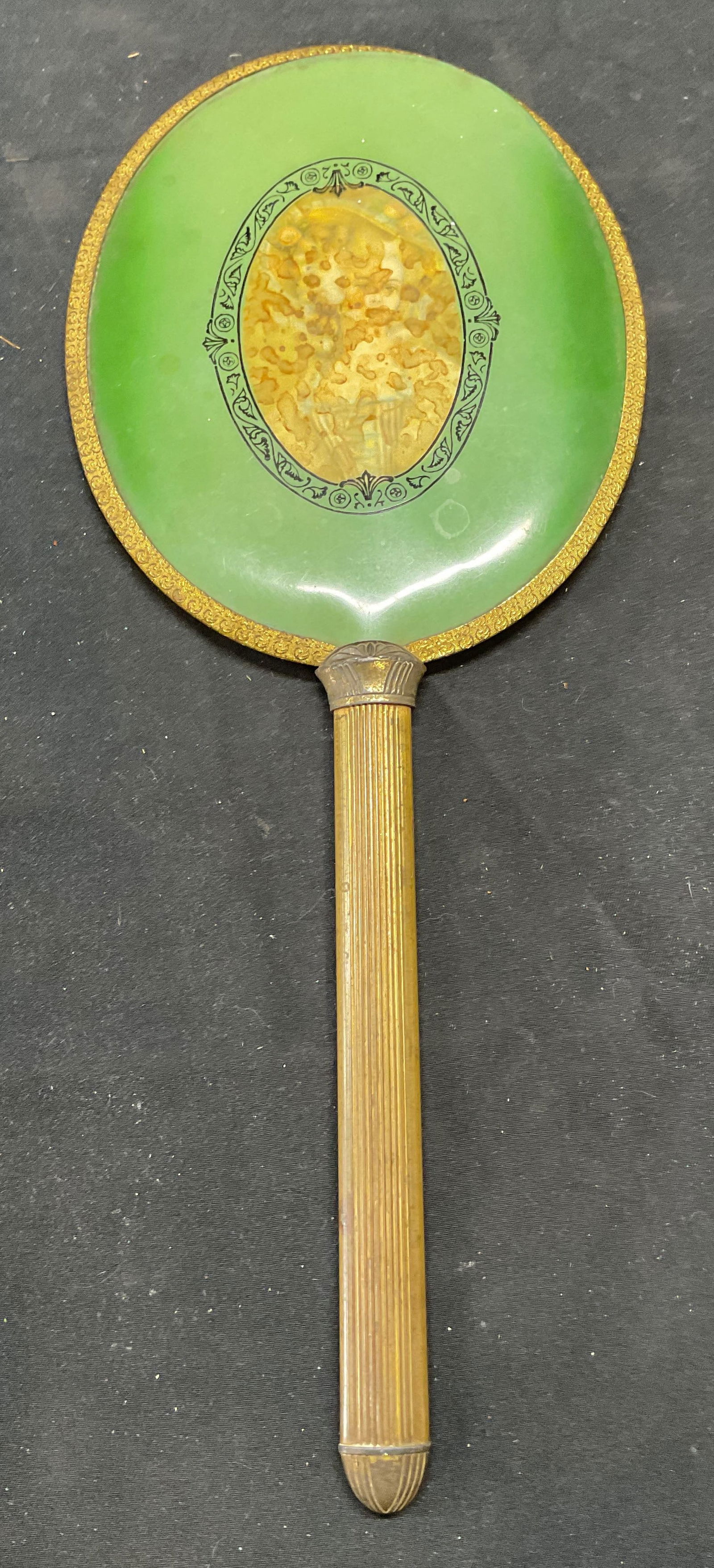 Vintage Brass Green Portrait Hand Mirror: Vintage brass handle hand mirror with green backing and portrait of woman. Possibly celluloid. Measures approx. 12.25 x 5 inches. Surface wear including scratching and discoloration observed. Mirror,