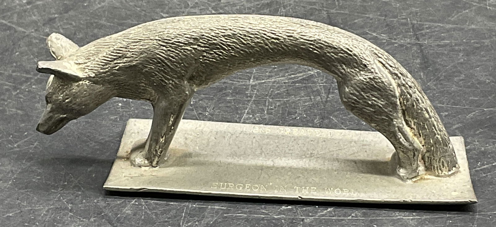 Sheffield English Pewter Fox Figural: A pewter fox figural. Base reads 2nd Greatest Surgeon In The Wild. Measures approx. 1.5H x 4W in. Measured at widest point. Underside signed Sheffield English Pewter. Some surface wear consistent with