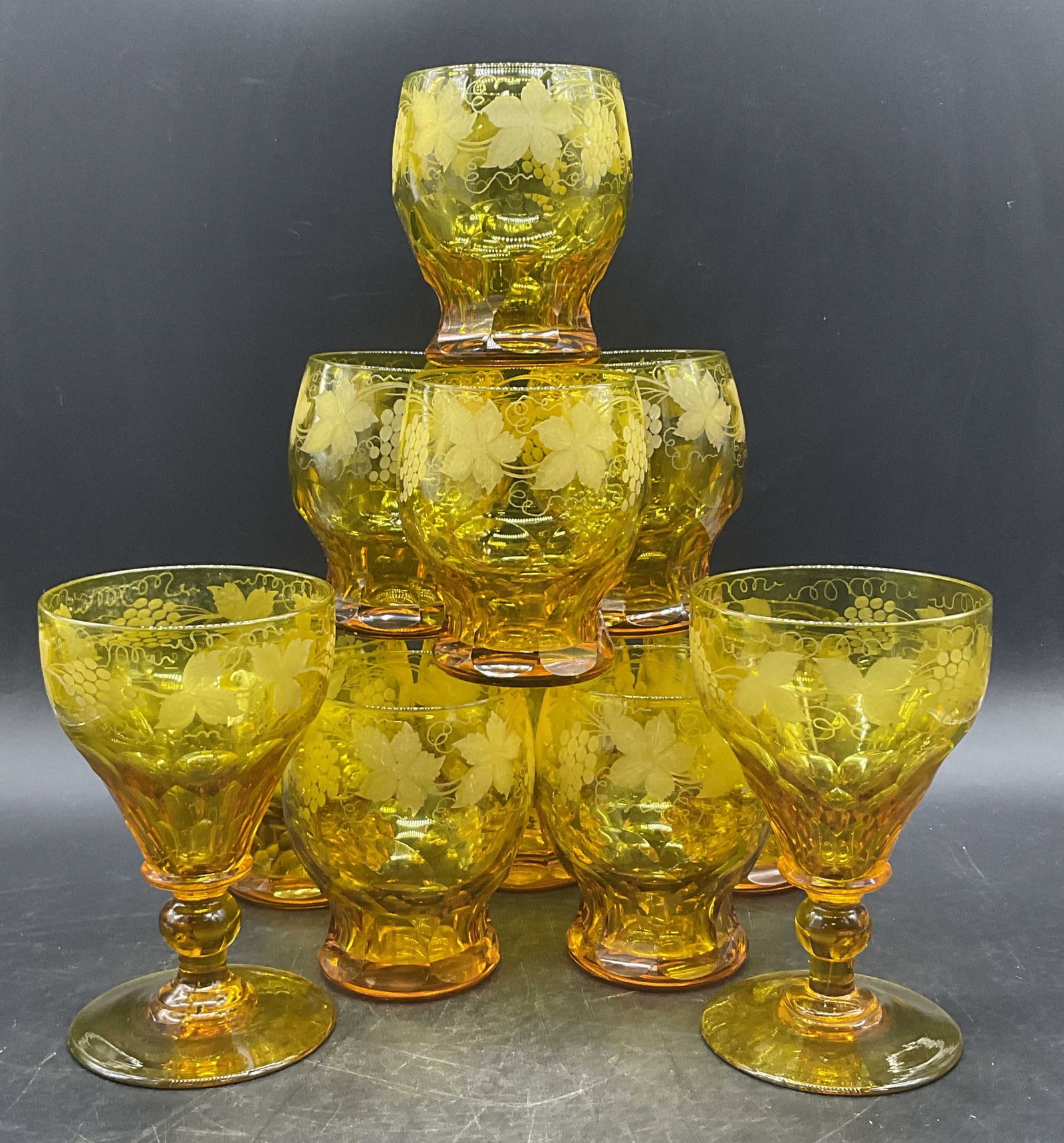 Set 11 Vintage Yellow Bohemian Crystal Glasses: A set of vintage yellow bohemian crystal glasses featuring frosted grape vine motifs. Faceted details to the crystal. Lot includes water glasses and wine glasses. The wine glasses measure approx. 6H x