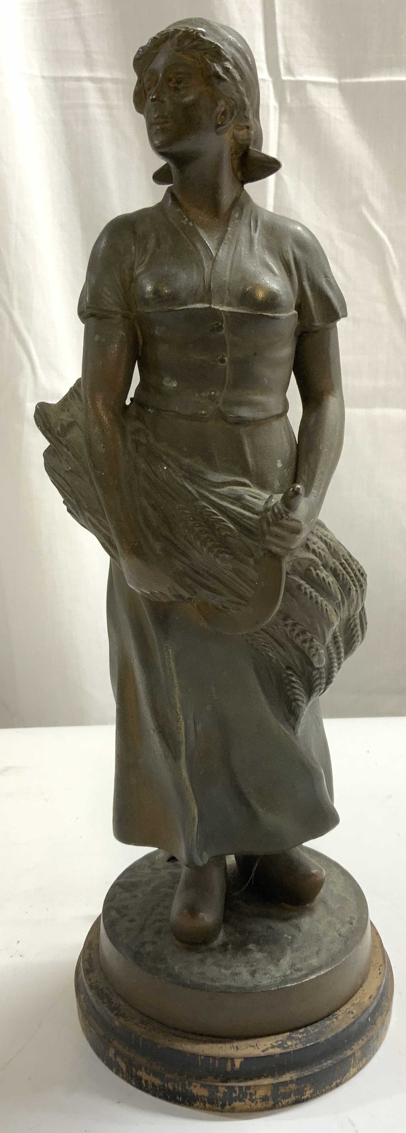 Gilt Metal Dutch Woman Figure GERMANY: Base is inscribed GERMANY. Piece depicting a standing Dutch female figure carrying wheat, wearing clogs. Piece has circular form black toned wooden base. Figure is gilt metal possibly brass. Piece mea