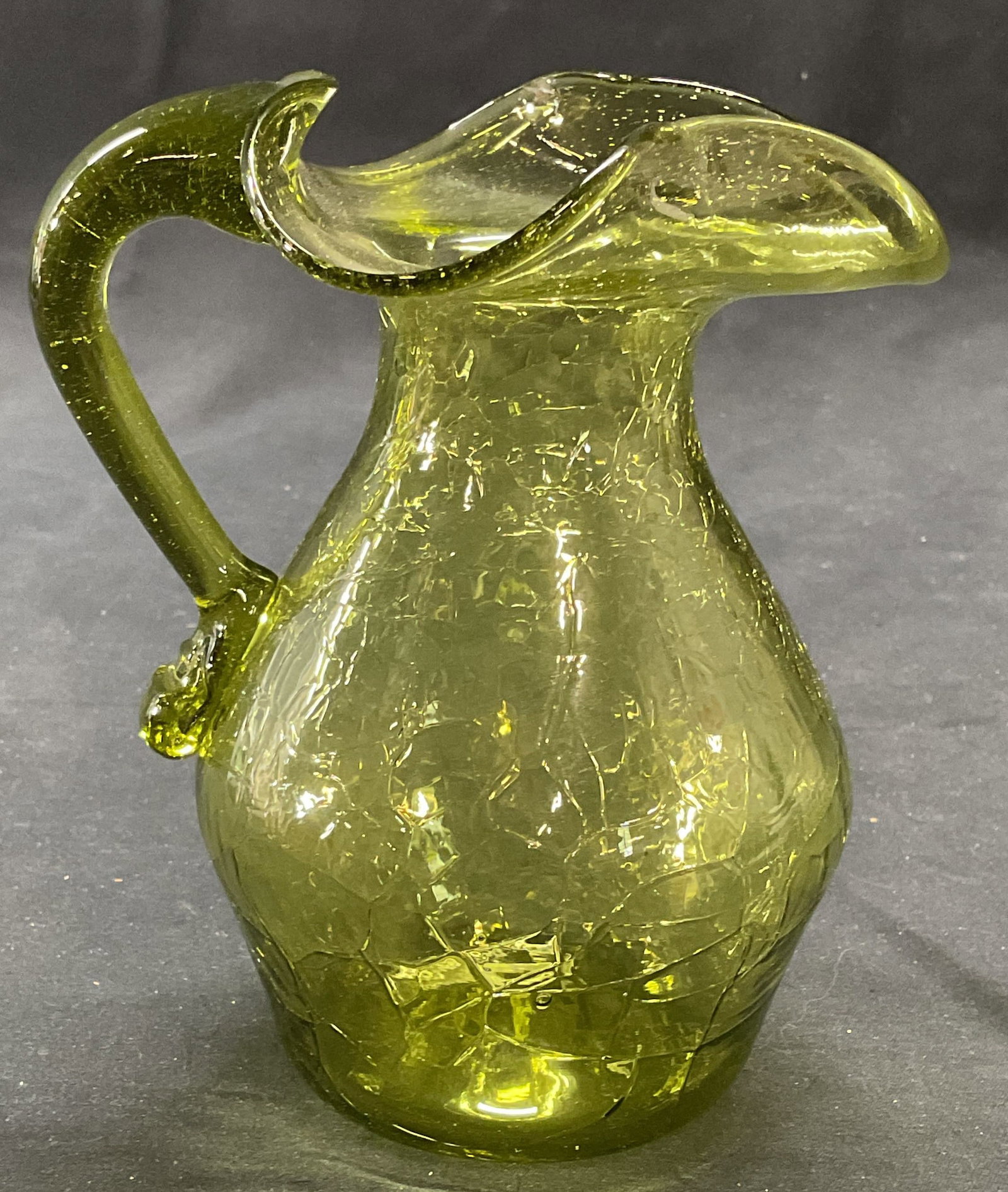 Hand Blown Green Art Glass Pitcher: Hand blown green art glass pitcher with handkerchief rim. Crackle glass pattern. Measures approx. 4.75 x 4 x 5.5 inches. Some surface wear including scratching observed. Pitcher, art glass pitcher, gr