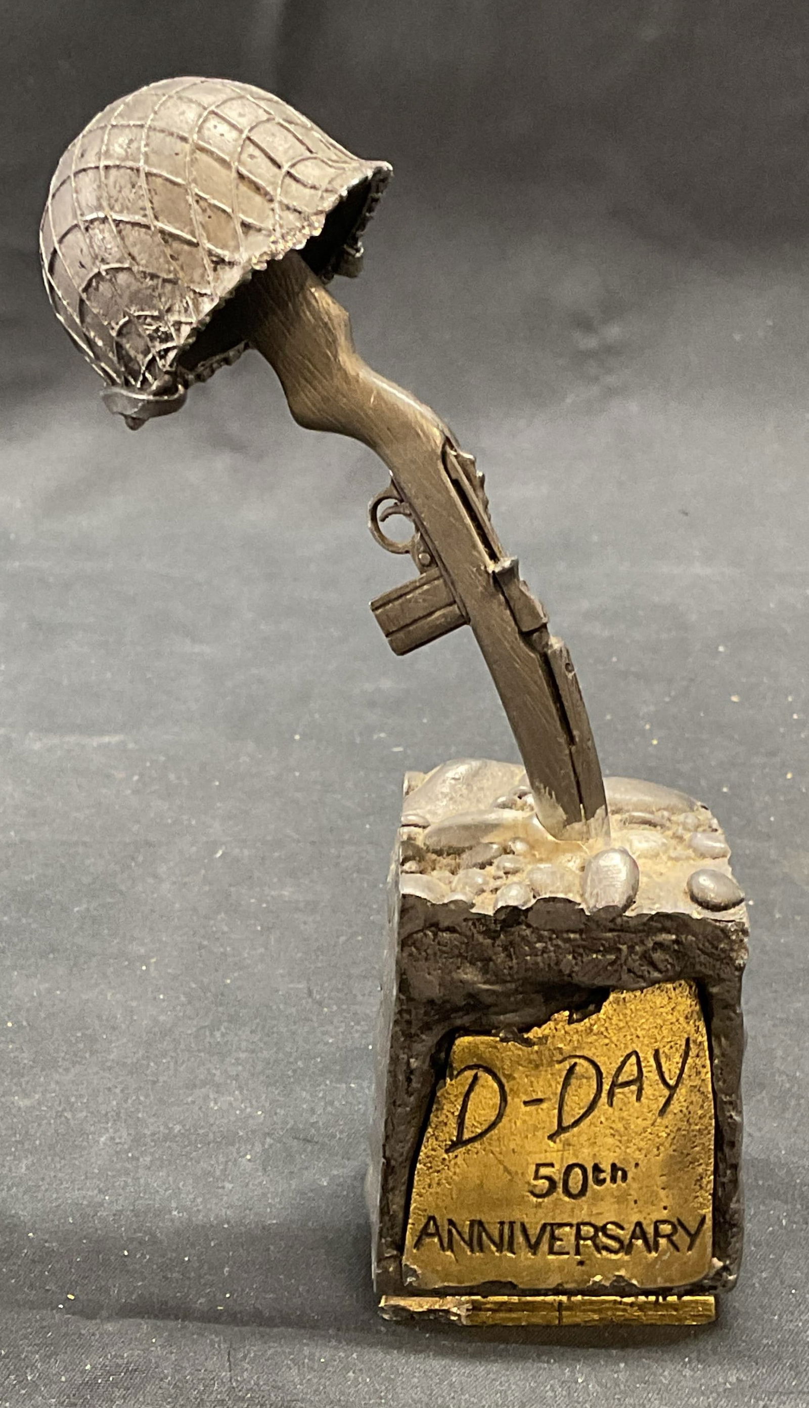 Zach Walinski D Day 50th Anniversary Sculpture: Signed Zach Walinski D Day 50th Anniversary metal sculpture. Possibly pewter. Depicts soldiers helmet and gun. Signed on reverse. Piece has weight. Measures approx. 6 inches tall. Some surface wear in
