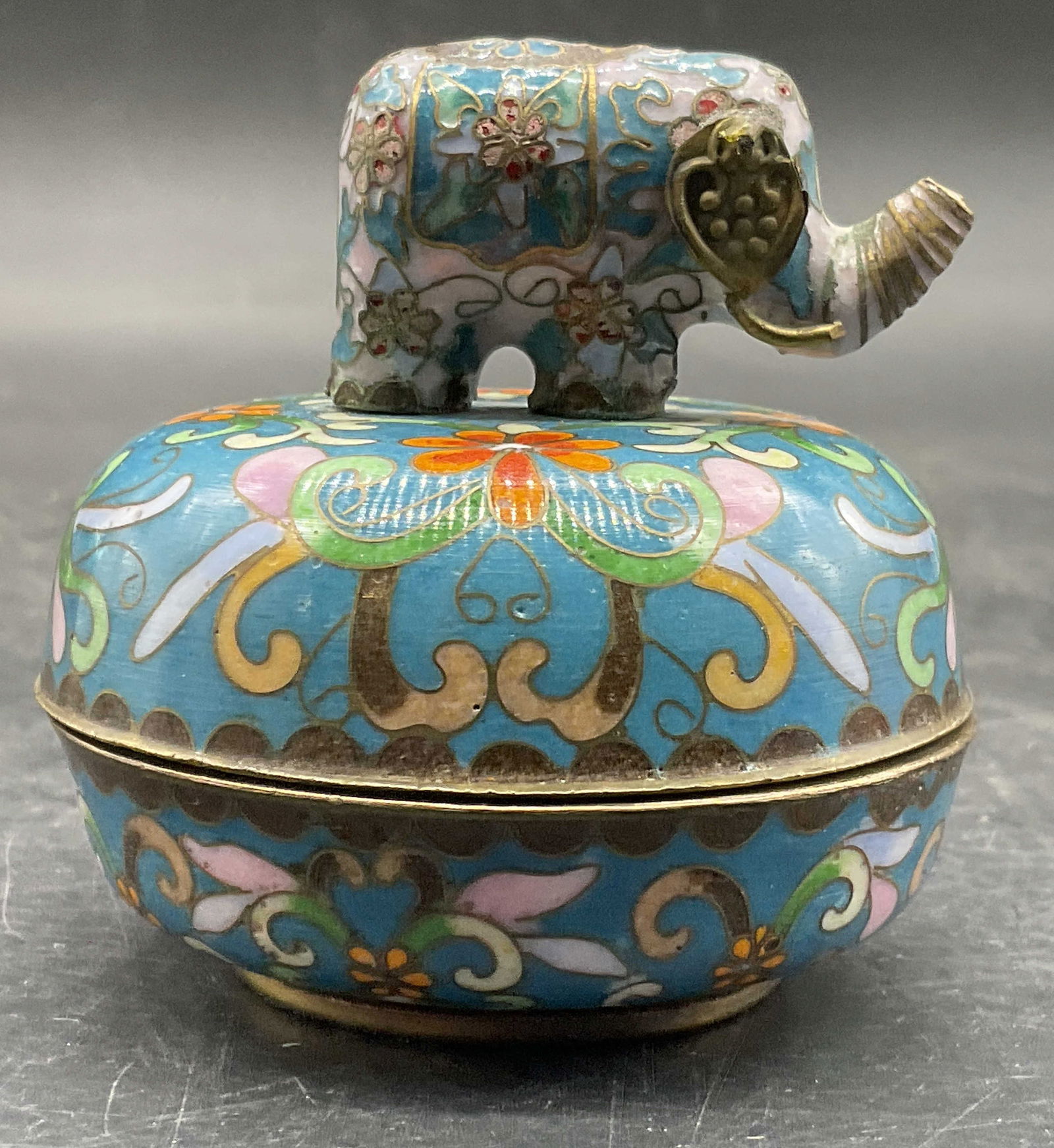 ARDLEIGH ELLIOT Sgnd Cloisonne Music Box 1992: A vintage musical cloisonne trinket box with an elephant figural to the lid. Multicolored florals and geometric shapes to the design. The underside is signed with Asian characters and reads 1992 ARDLE