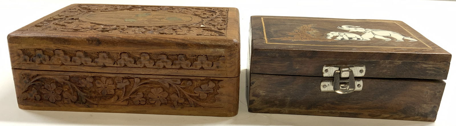 Lot 2 Carved Wooden Keepsake Boxes W Lids: Lot includes 2 keepsake boxes. One has white toned bone inlay depicting elephants, one has intricate floral, & leaf carved relief detail & gilt metal inlay detail to center of lid. Each box has hinged