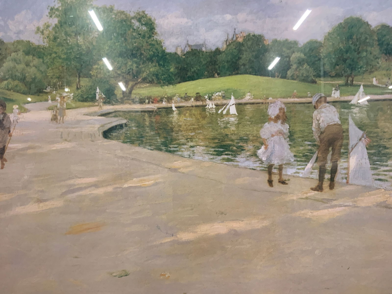 After William Merritt Chase Miniature Yachts Litho: Lithograph on paper. Art after William Merritt Chase. Titled The Lake for Miniature Yachts. Subject depicts a lake filled with small sailing boats and people walking by, a little girl and boy are abou