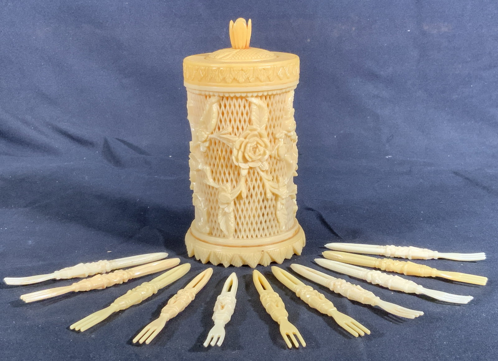 Composite Lace Hors D oeuvres Forks & Container: 38 composite Hors D Oeuvres forks in composite container. Container has lace and rose motif with foliage motifs on lid and base. Each fork has three prongs and a scrolling motif on handle. Container m