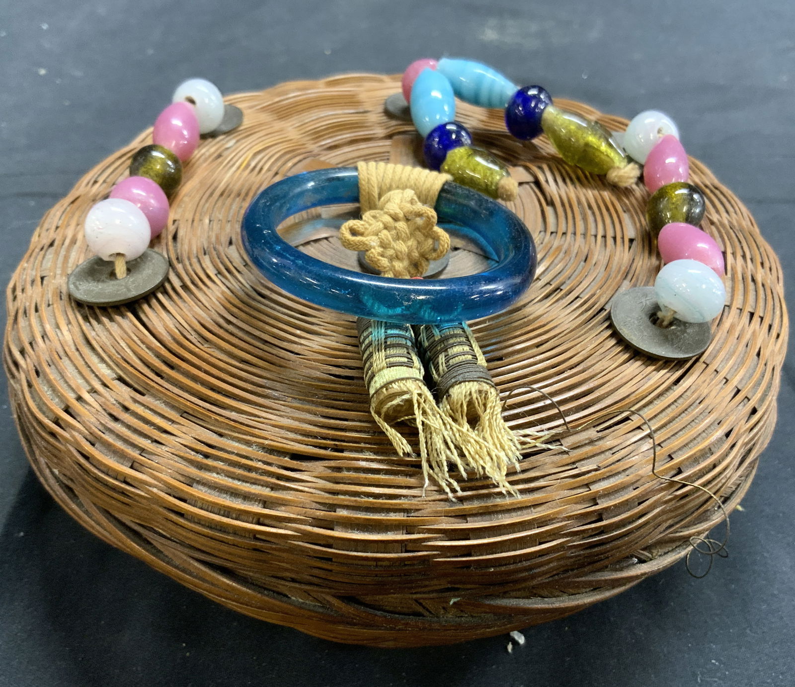 Beaded Woven Wicker Keepsake Box W Lid: Keepsake box is brown toned woven wicker. Piece includes lid. Box has multi toned beaded detail at top with turquoise toned loop handle. Piece has circular form. Box measures approximately 6 inches di