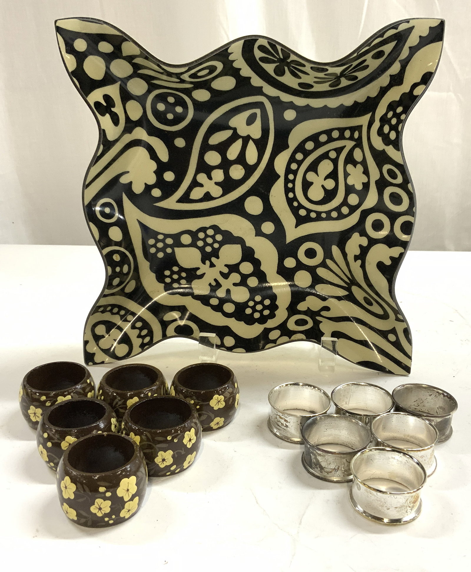 Lot 13 Acrylic Handkerchief Bowl & Napkin Rings: Lot includes 6 white metal napkin rings, 6 brown toned hand painted napkin rings with floral & leaf detail & 1 acrylic handkerchief bowl. Bowl is black & cream toned with leaf & geometric detail. Bowl