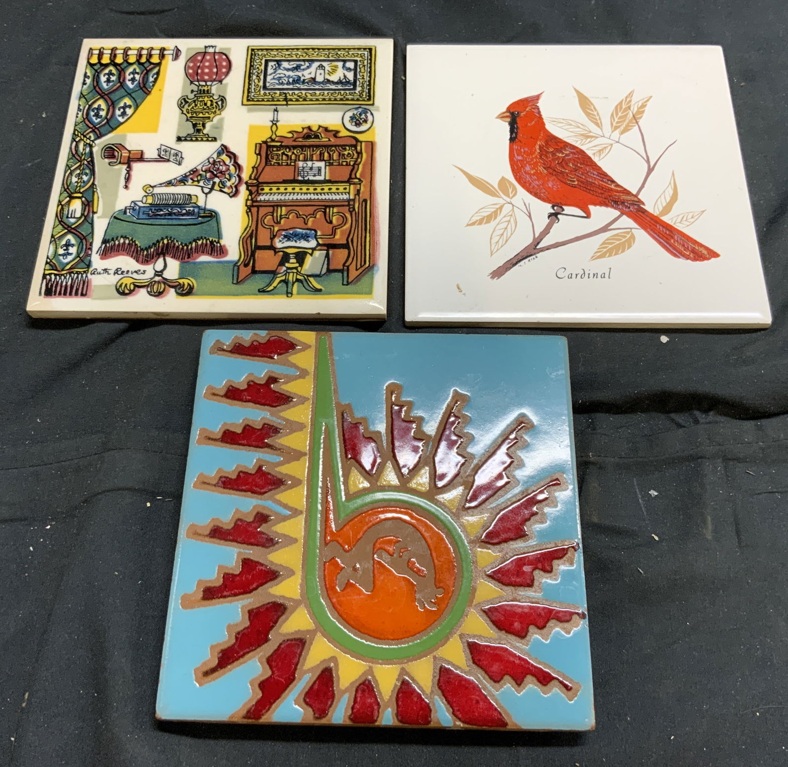 Lot 3 Assorted Porcelain Tile Trivets: Lot includes 1 tile with image of Cardinal, 1 tile with multi toned image of room and objects within room & 1 tile with multi toned geometric detail. Largest tile measures approximately 6 inches squar
