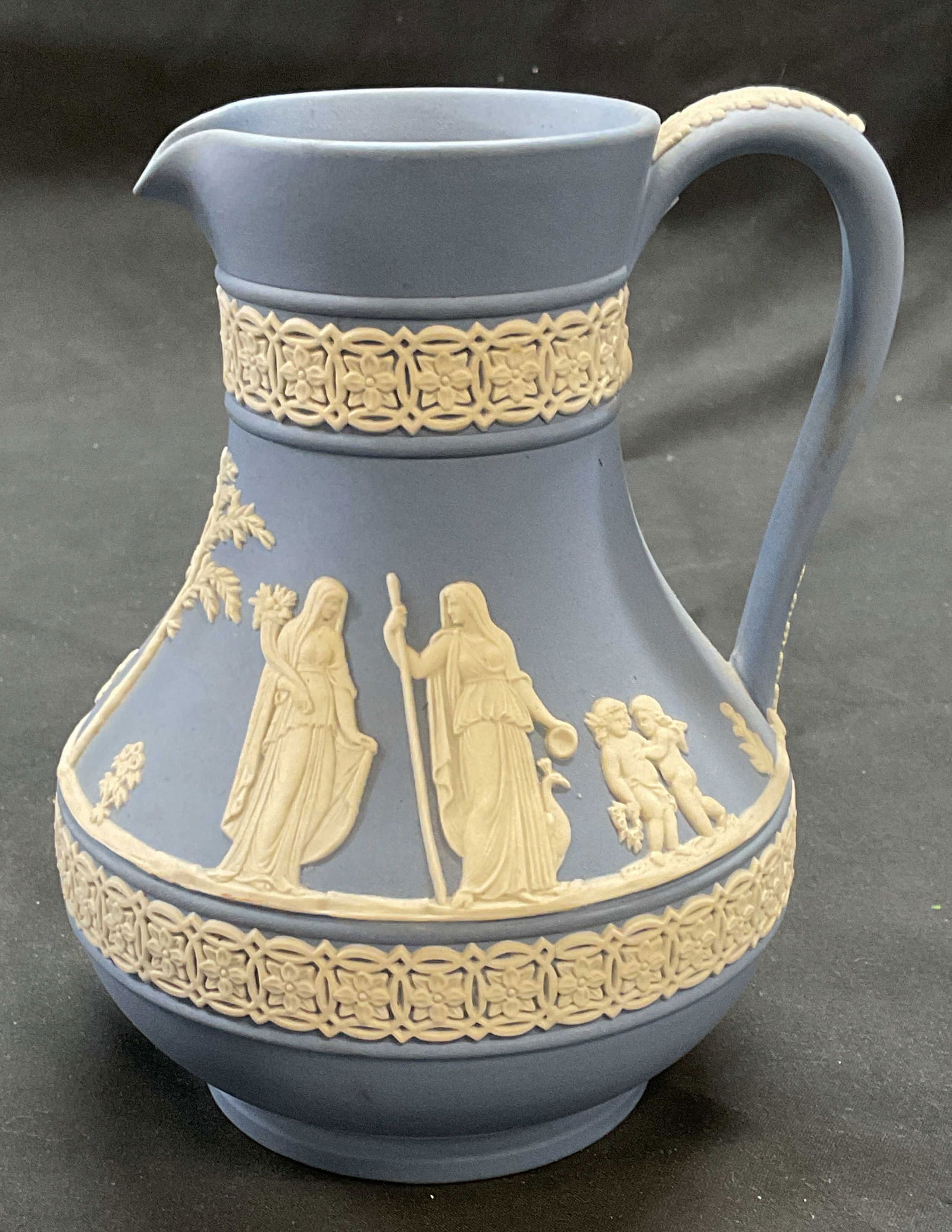 Vntg Wedgwood Blue Jasperware Pitcher, England: Vintage Wedgwood blue Jasperware pitcher with white bas relief classical scene decoration. Signed on underside. Made in England. Measures approx. 4.5 x 6 inches. Some surface wear including scratching