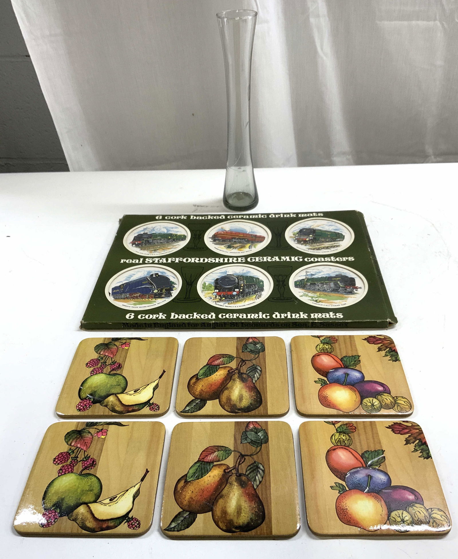 Lot 13 Coasters & Glass Vase W Boxes: Lot includes 6 fruit detailed cork coasters 6 STAFFORDSHIRE Ceramic coasters with original box & FLORA glass Bud vase with original box. Vase has frosted floral detail. Vase measures approximately 10