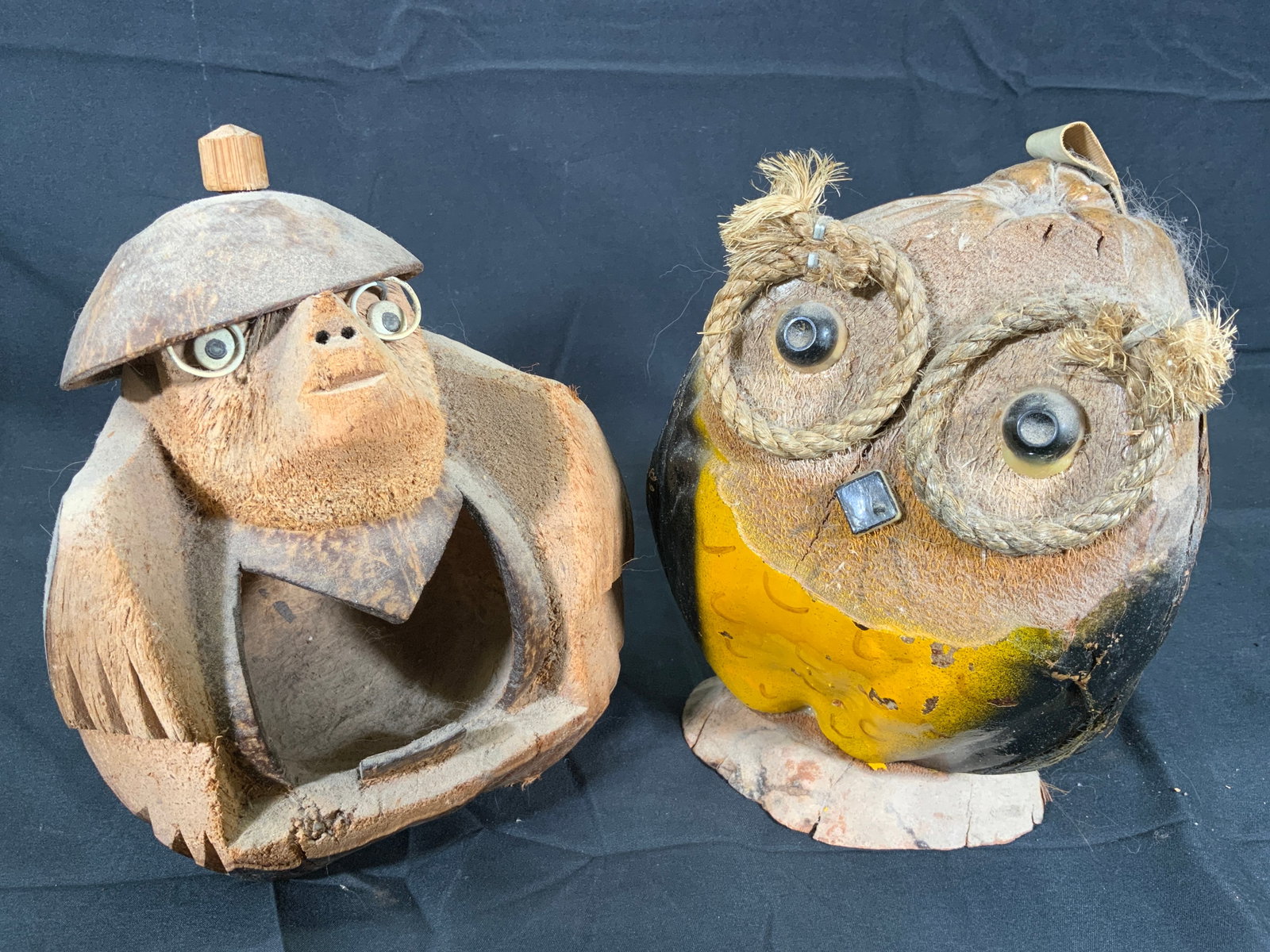 Coconut Folk Art Statues Monkey & Owl Pair: Two coconut sculptures. Subject depicts a folk art style monkey with glasses and a hate on, coconut is hollowed out. Other subject depicts an Owl coconut. Larger sculpture measures approx. 5 W x 7.5 H