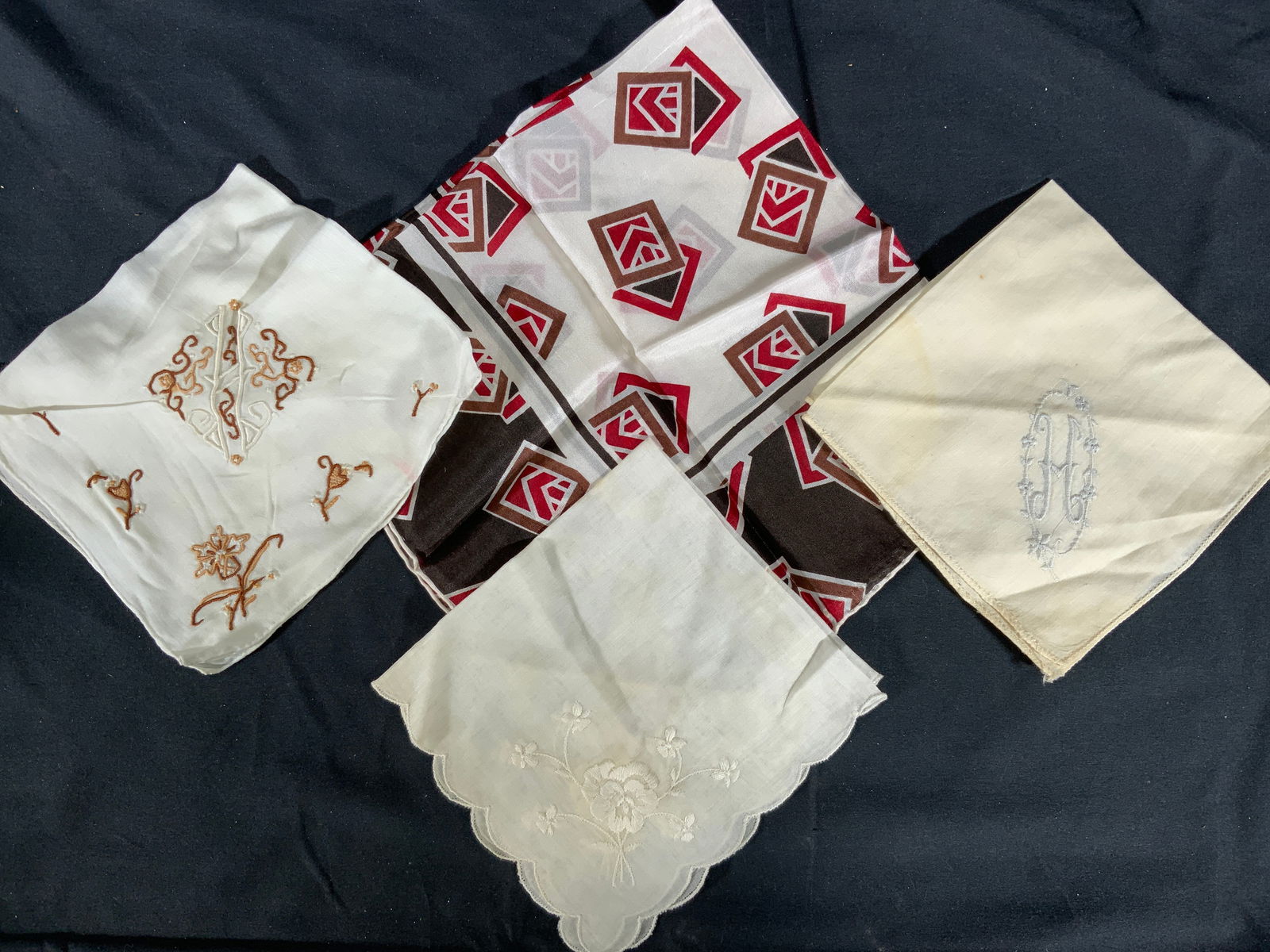 Lot 4 Handkerchiefs Silk & Embroidered Linens: Lot 4 Handkerchiefs. One silk handkerchief with a geometric patterned motif in red, brown and white. Measures approx. 17 x 17 in. White linen handkerchief with scalloped edges and a white floral embro