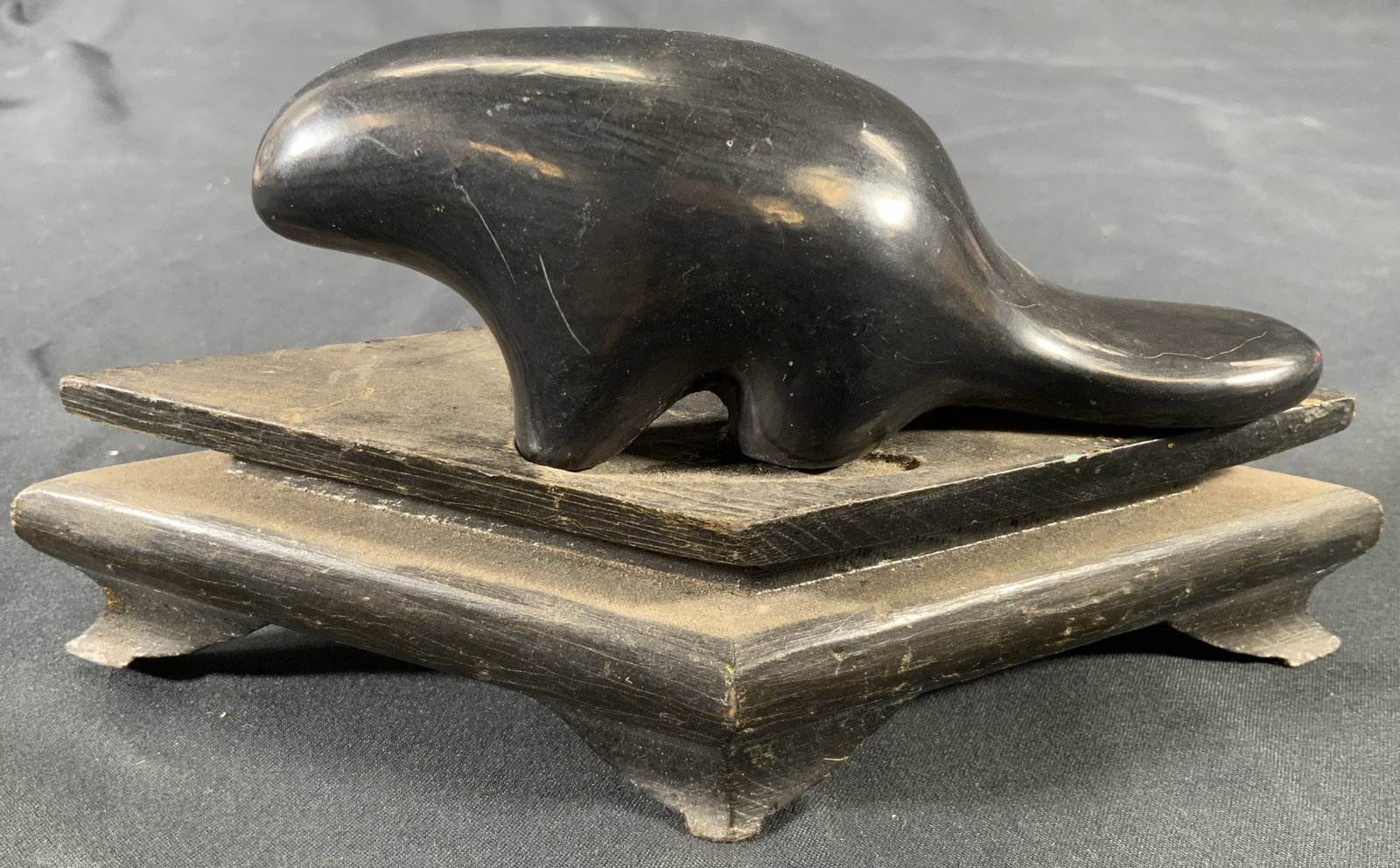 Ceramic Beaver Figural on Wooden Platform: Ceramic figural on wooden platform base. Ceramic figural depicts a beaver. Figure is on top of a black wooden platform. Platform measures approx. 7 W x 3 D x 1.5 H in. Beaver figural measures approx. 
