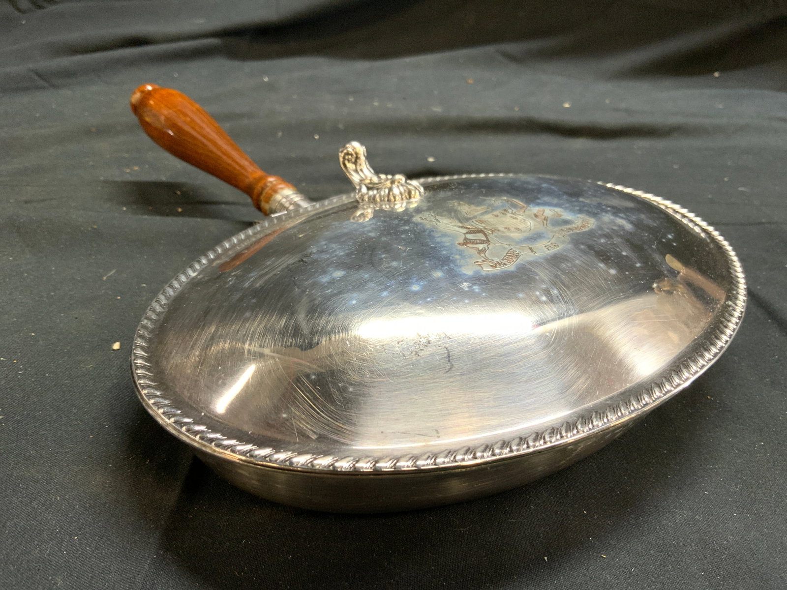 FB RODGERS Silver On Copper Crumb Catcher W Lid: Underside is inscribed FB RODGERS SILVER CO SILVER ON COPPER. Lid is monogrammed MAJOR AB ADVERSIS with coat of arms and horse detail. Crumb catcher has lid. Piece has light brown toned wooden handle.
