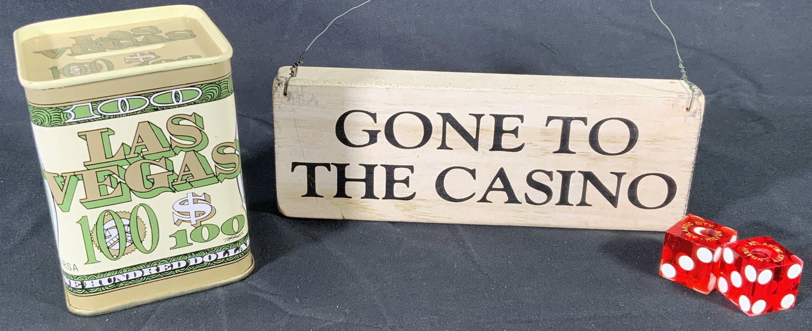 Assorted Casino Group Lot Dice, Money Bank, Sign: Assorted Casino Themed Items. Wooden sign reads Gone to the Casino. Wore affixed to wood for hanging purposes. Money bank depicts a one hundred bill on side and reads Las Vegas. Mindy bank measures ap