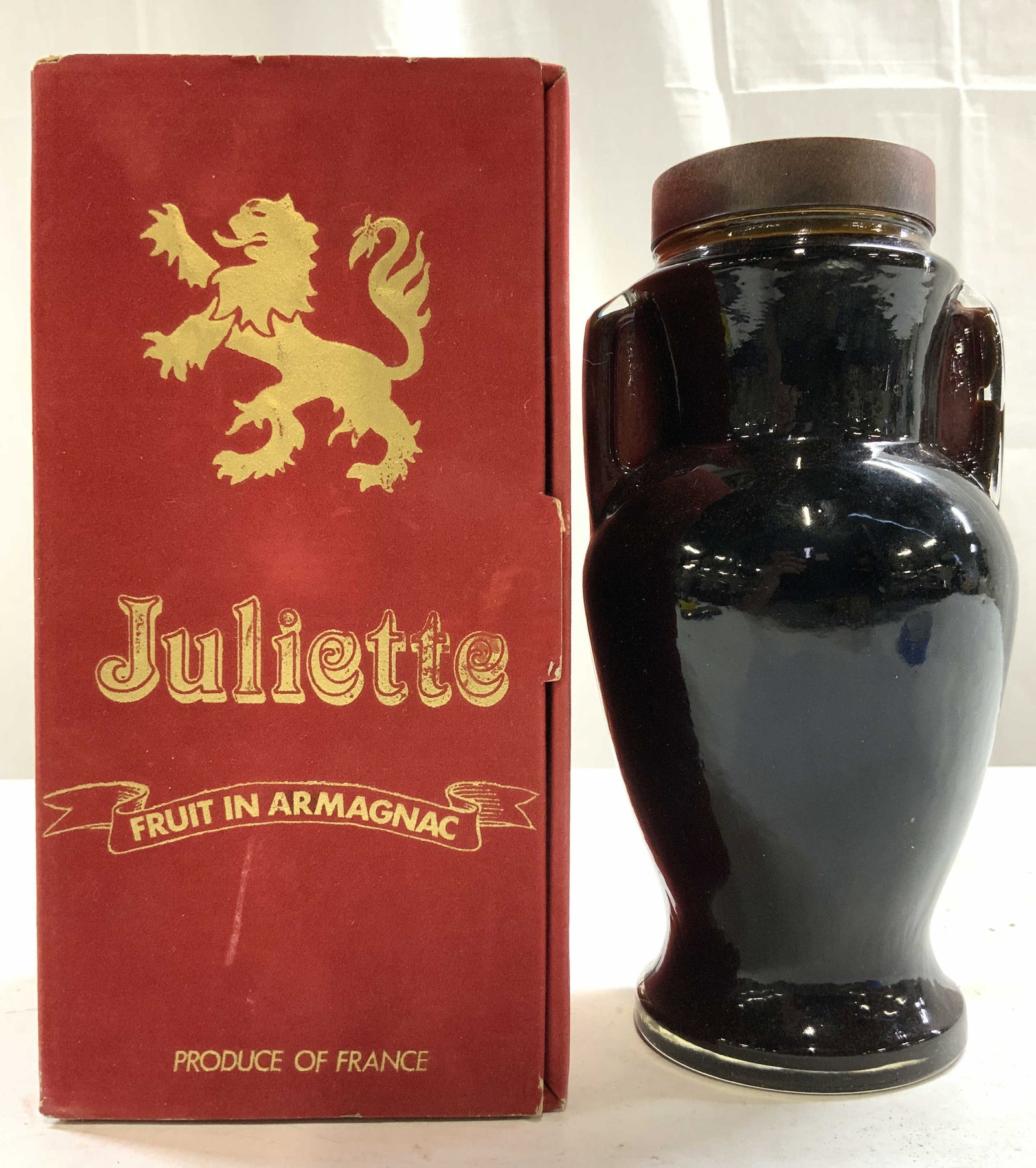 JULIETTE FRUIT IN ARMAGNAC Bottle W Box: Box is red toned with gilt griffin detail and lettering which reads JULIETTE FRUIT IN ARMAGNAC PRODUCE OF FRANCE. Bottle has urn shape and includes brown toned lid. Bottle measures approximately 8 inc