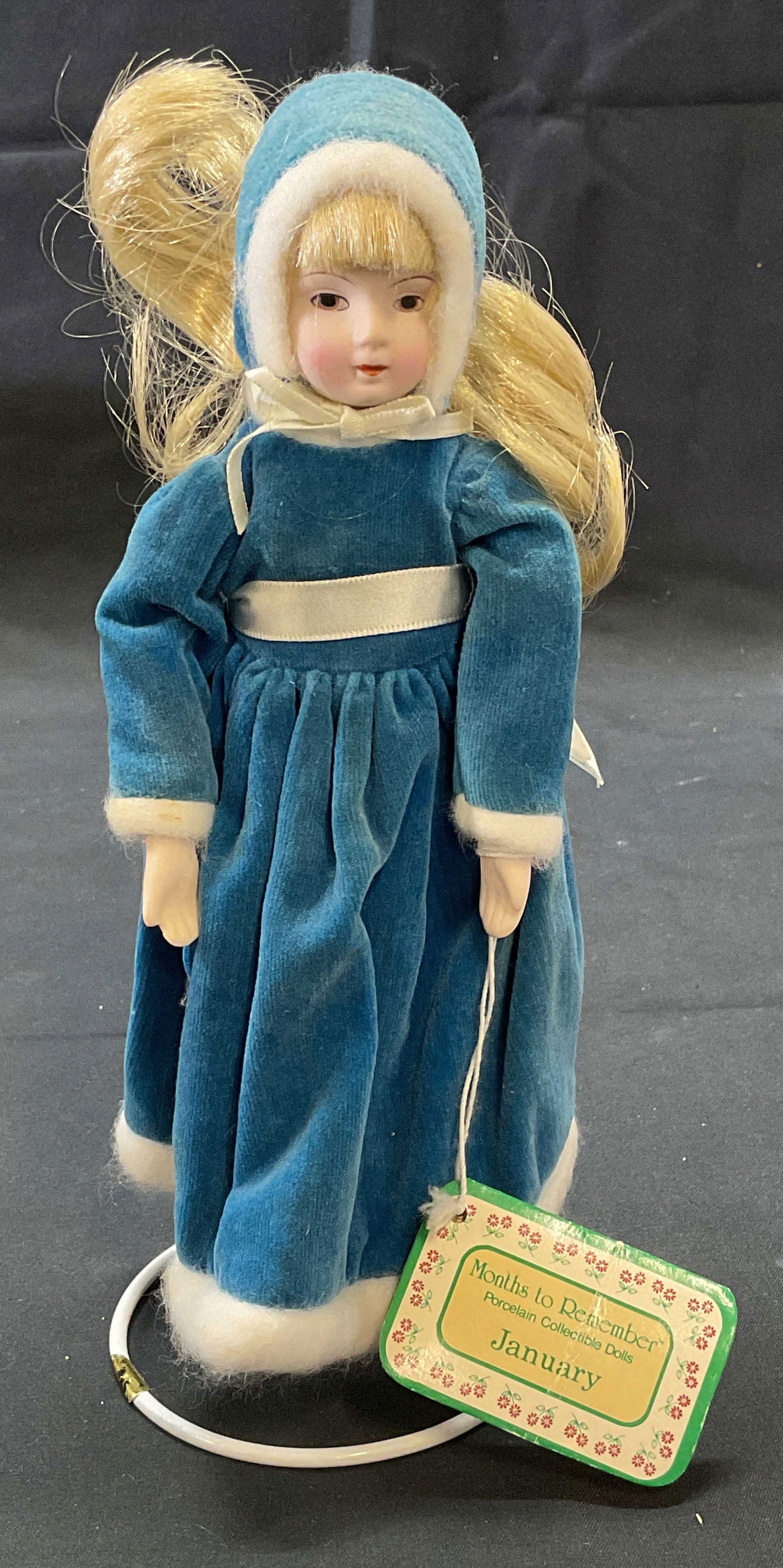 Months To Remember January Porcelain Doll: Months to Remember January collectible porcelain doll. Porcelain and fabric. Blue velvet dress. Measures approx. 8.5 inches tall. Includes doll stand. Some wear to material consistent with exposure. M