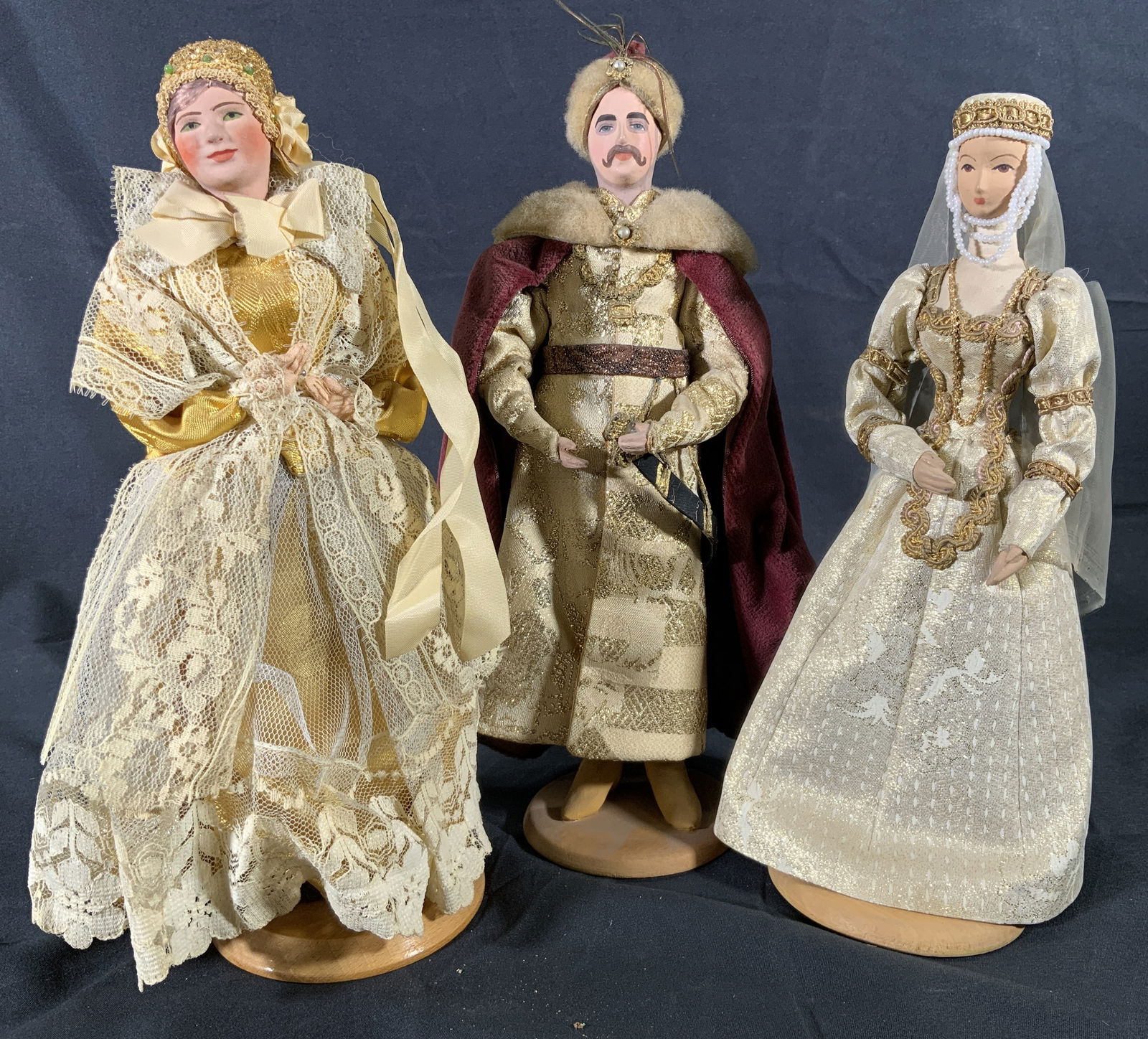Three Traditionally Dressed Polish Dolls: Three wooden and fabric dolls on stand. Dolls are wearing traditional polish cultural dresses and suit. Undersides of stand have provenance. Tallest doll measures approx. 4 W x 10.5 H in. Minor wear t