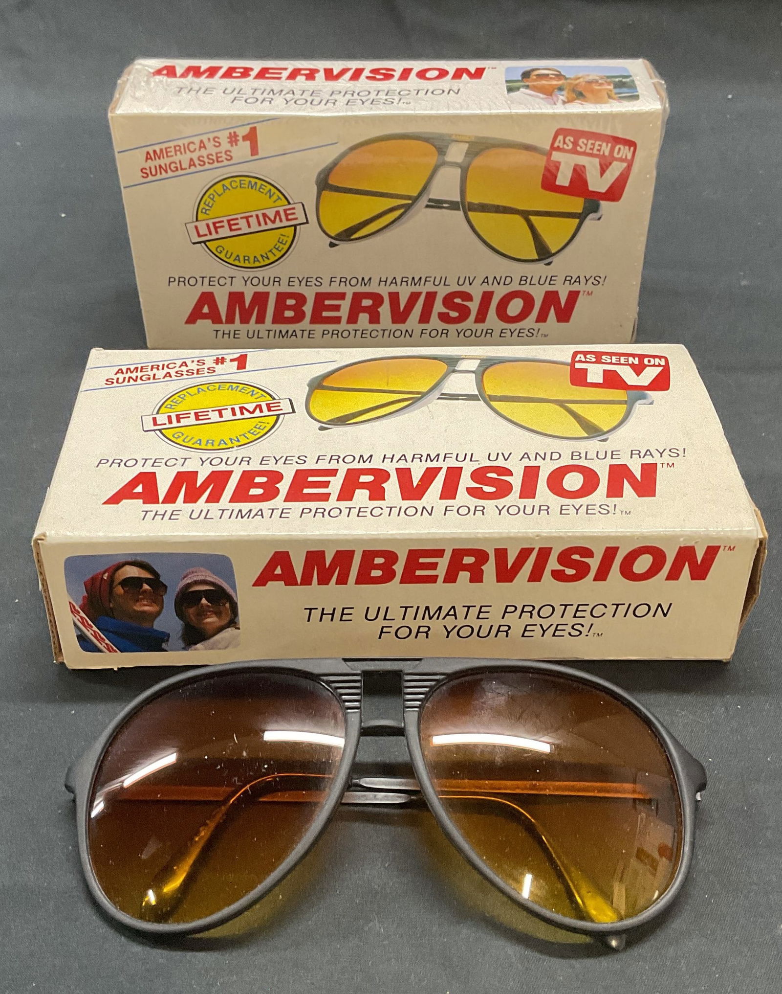 Pair Ambervision Sunglasses NIB: Pair of Ambervision sunglasses. One pair is new in sealed box. Sunglasses measure approx. 5.5 inches wide, arm approx. 5 inches long. Composed of plastic and metal. Both pieces have some wear consiste