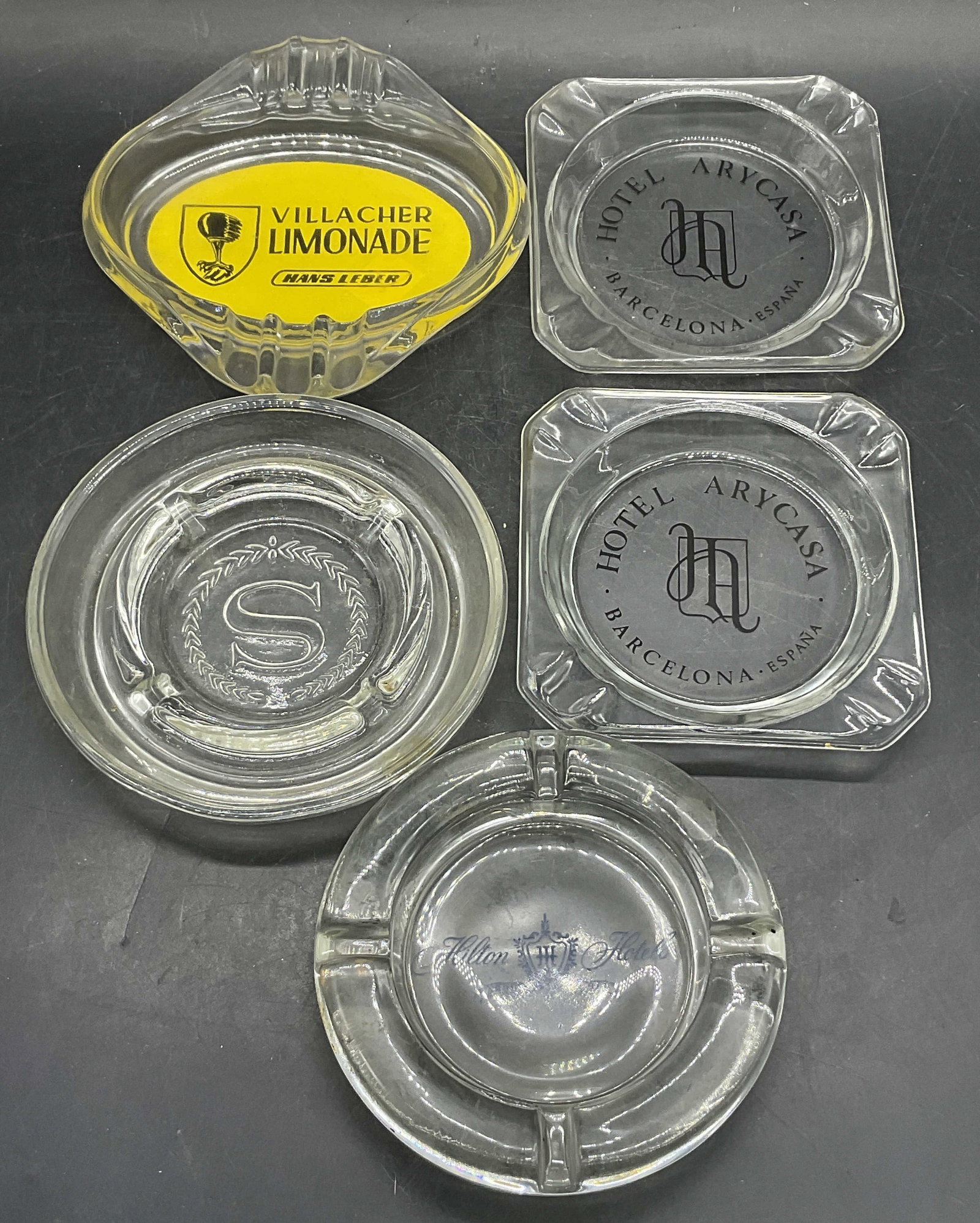 Lot 5 Restaurant & Hotel Glass Ashtrays, Hilton +: Four restaurant and hotel glass ashtrays / trinket dishes. Pieces feature names or symbols to their centers. Some read: HOTEL ARYCASA, HILTON HOTELS, and more. Sheraton Ashtray with the letter S to th