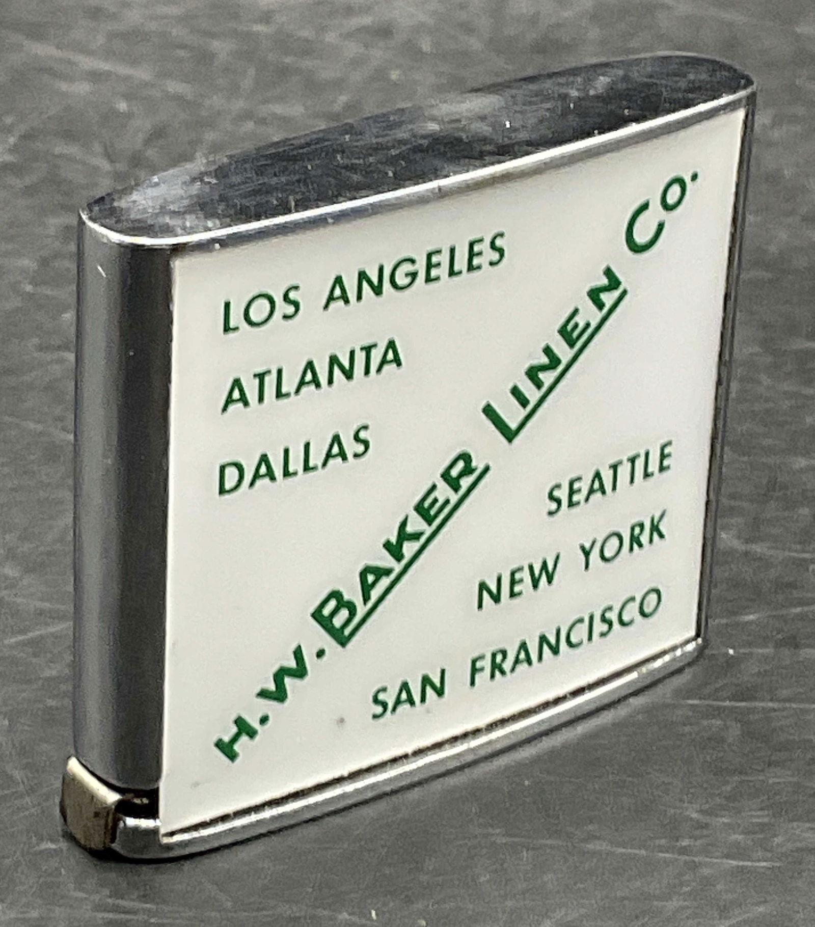 HW BAKER LINEN CO. BARLOW Tape Measure: A HW BAKER LINEN CO. BARLOW Tape Measure. Crafted from silver tone metal. Obverse reads HW BAKER LINEN CO. Underside reads BARLOW. Tape reads BARLOW, MADE IN USA. Measures approx. 1.75L x 2W in. Sone