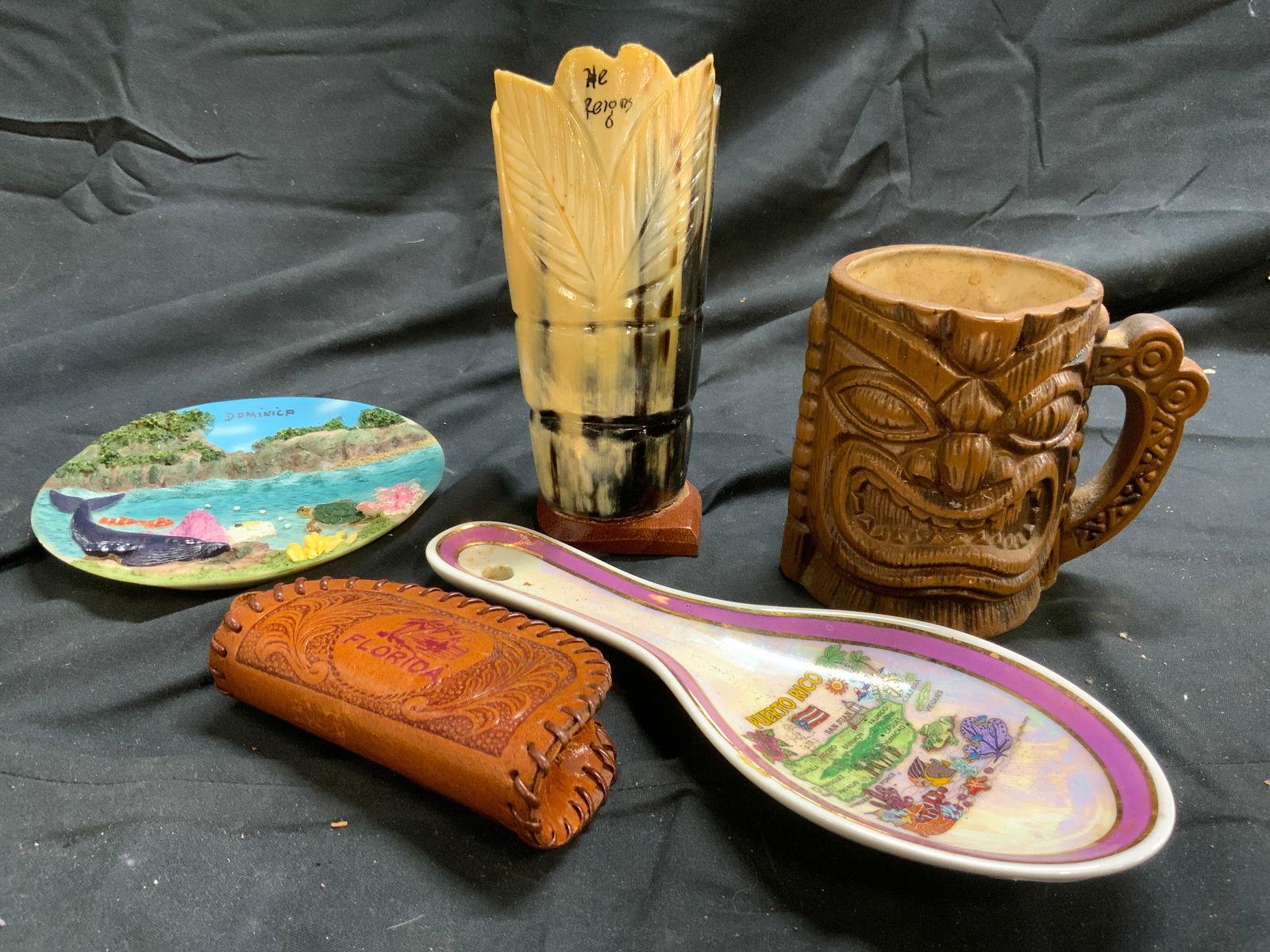 Lot 5 Tabletop Decor, Puerto Rico, Dominica & More: Lot includes 1 resinous tiki mug, 1 PUERTO RICO porcelain Ladle holder, 1 FLORIDA Leather coin pouch with zipper, 1 DOMINICA Resin plate, & 1 vessel which appears to possibly be carved bone. Ladle hol