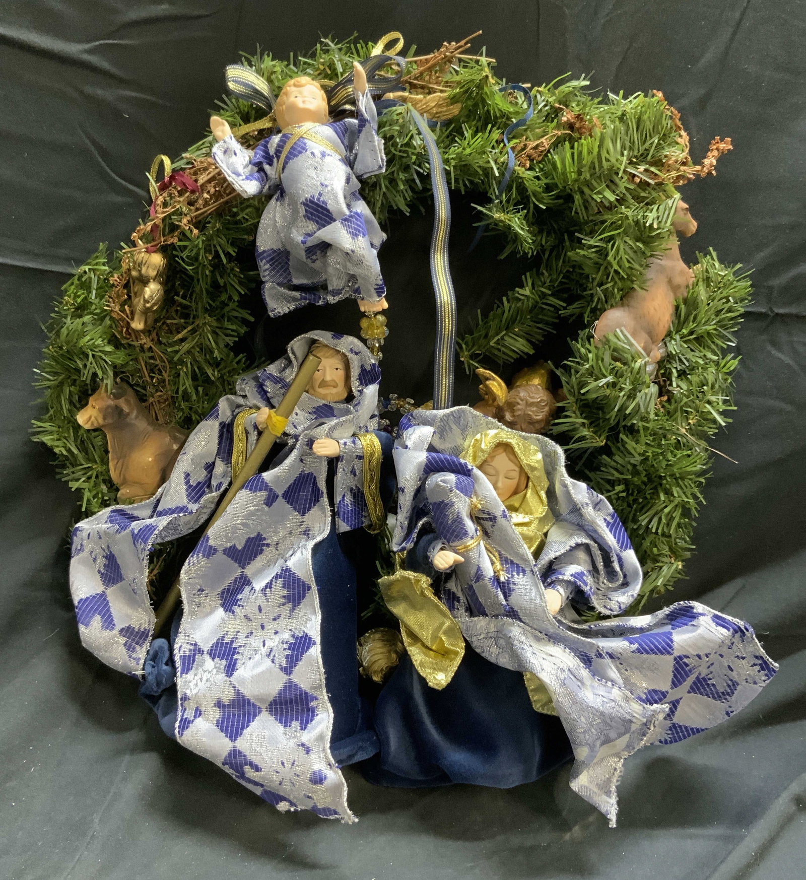 Nativity Christmas Wreath Holiday Decor: Wreath has male and female figure, cherub figures, horse & cow figures. Figures are wearing navy, ice blue & gold toned clothing. Wreath has some twigs detail throughout. Wreath measures approximately