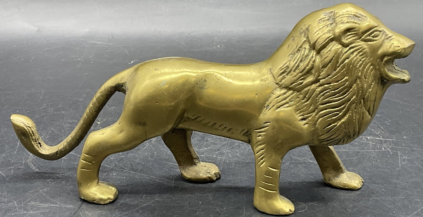 Vintage Gilt Metal Standing Lion Figural: A vintage gilt metal standing lion figural. The lion is depicted with their mouth open. Measures approx. 4H x 7.75W in. Patina. Seam present. Discoloration and surface wear to the piece. home decor, h