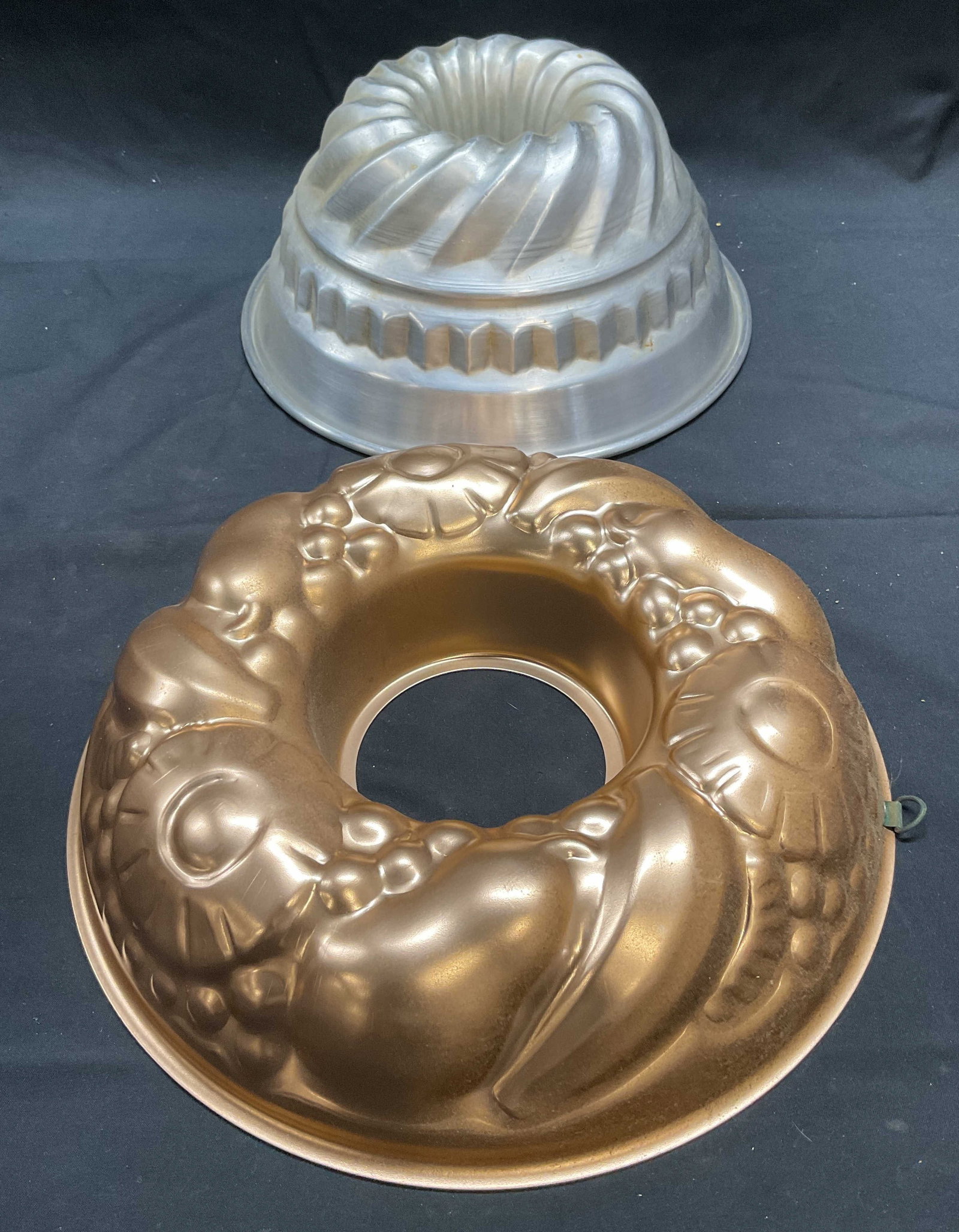 Lot 2 Vintage Metal Food Molds: Lot of 2 vintage silver tone and copper food molds. Floral and fruit motif and swirl pattern. Larger piece measures approx. 10 x 2.5 inches. Both pieces have surface wear consistent with exposure. Mol