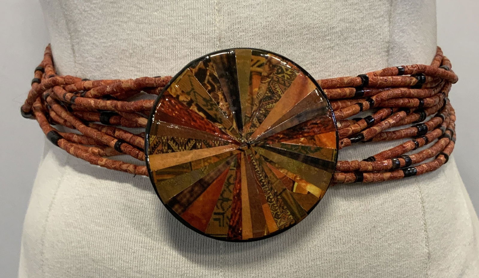 Coral beaded Waist Belt with Wooden Pendant: Beaded belt accessory. Beads on string are made of coral. Wooden pendant has gilt toned hook clasps for wearing on pendants verso. Wooden pendant has paper collage with different patterns on front. Be