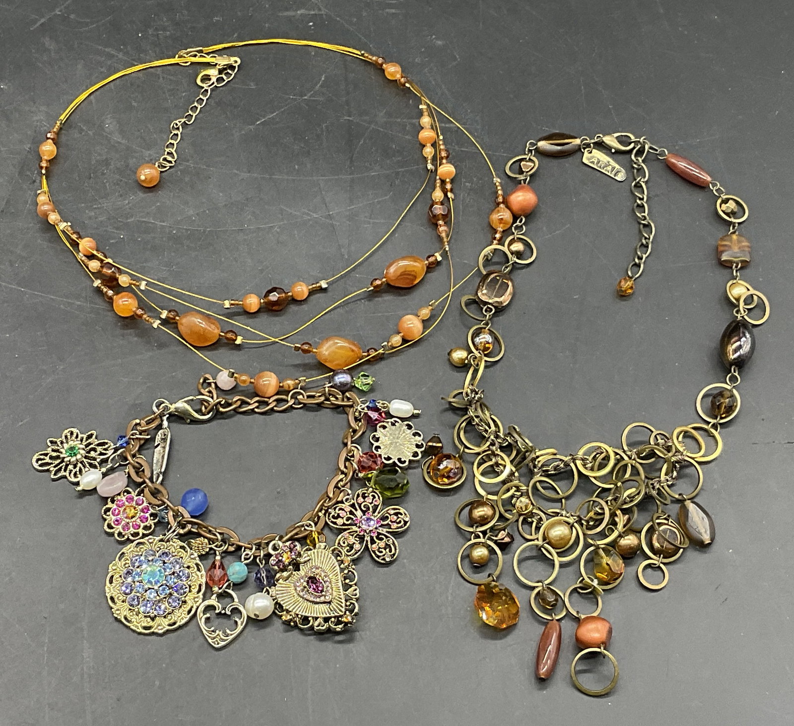 Lot 3 Bejeweled Necklaces & Bracelet, ANAT +: Two bejeweled necklaces and one bejeweled charm bracelet. The pieces feature faceted crystals in various colors, beads, charms, and more. All pieces secure with metal lobster clasp closures. One neckl