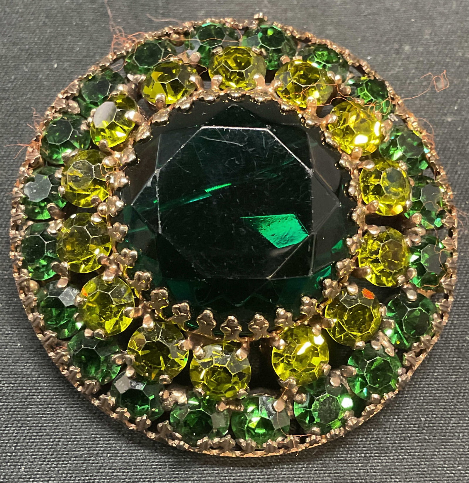 Vintage Weiss Gold Tone Green Crystal Brooch: Vintage Weiss gold tone round brooch with green crystal decoration. Signed on underside. Hinge pin on underside. Measures approx. 2 inches wide. Some surface wear including scratching observed. Jewelr