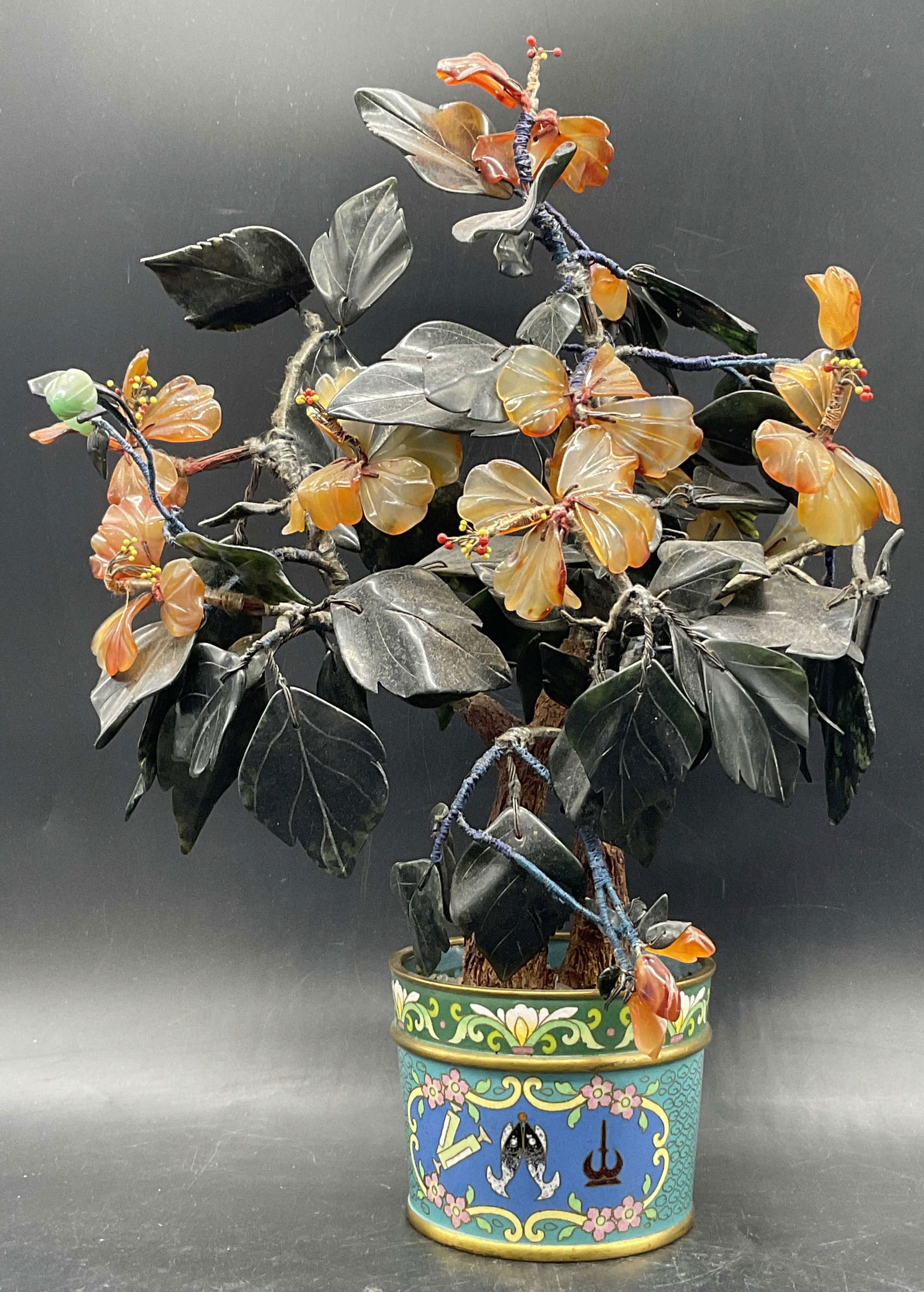 Natural Stone Tree In Cloisonne Planter 15in: A natural stone tree in a cloisonne planter. The flower petals and leaves are crafted from stone. The rest of the tree is crafted from fabric, wire, and plastic. The tree is affixed to a multicolored