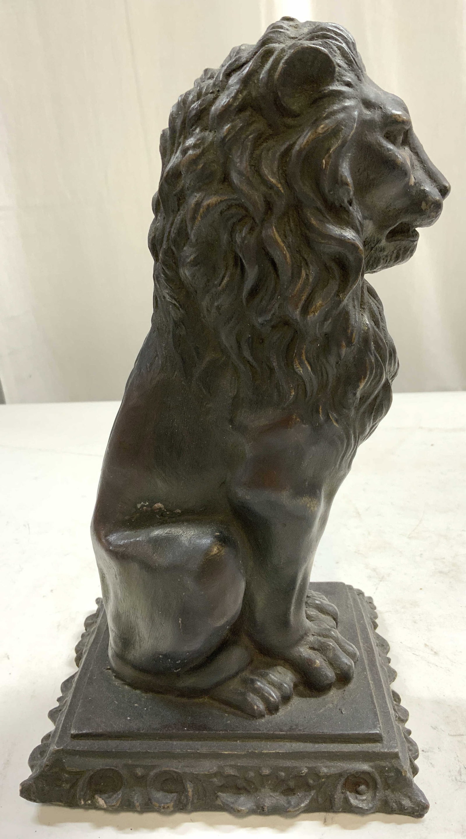 Resinous Seated Lion Figure Statuary 10.5in: Lion figure appears to be crafted from a resinous material. Piece is dark brown toned. Depicts a seated lion figure. Piece has rectangular shaped base with textured edges. Piece measures approximately