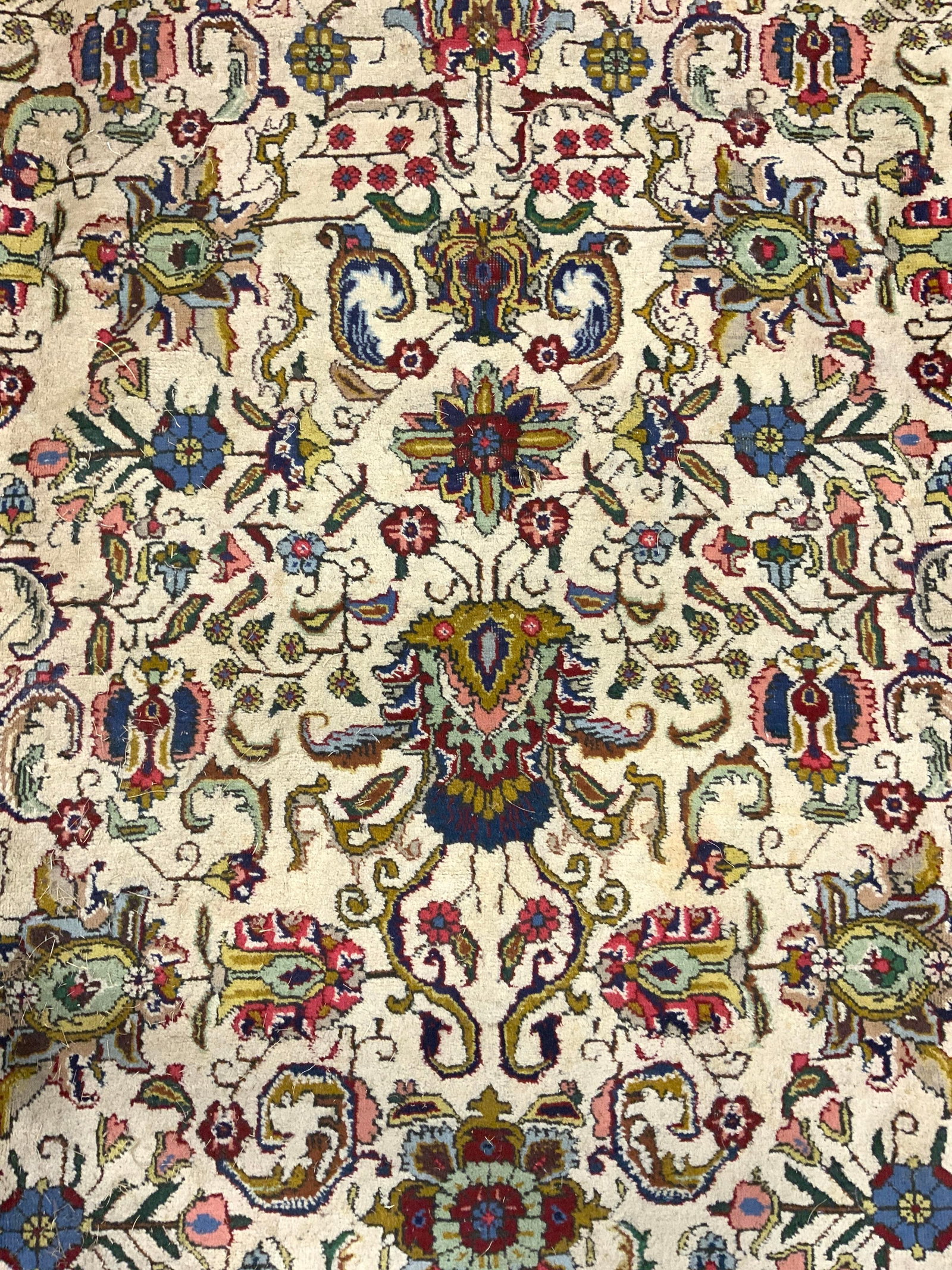 Vintage Handmade Oversized Fringed Wool Rug: Rug is handmade and wool. Piece is vintage. Rug is oversized. Piece has intricate multi toned floral, vine and leaf detail. Edges of rug have knotted sand toned fringes. Rug measures approx 163 inches