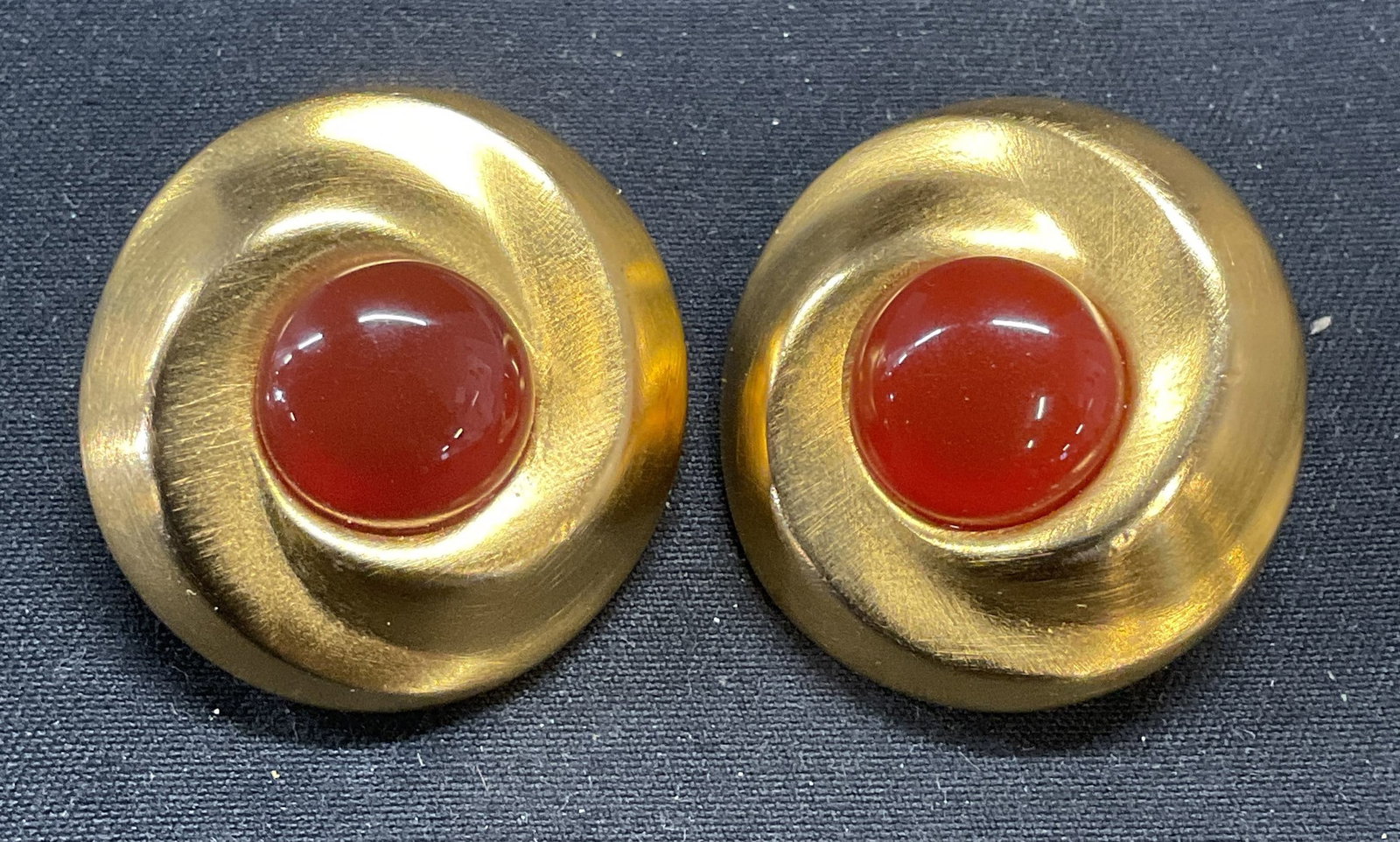 Vntg Clara Studio Asymmetry Gold Tn Earrings: Vintage 1994 Clara Studio for Asymmetry gold tone swirl earrings with faux carnelian cabochons. Signed and dated on undersides. Clip on backing. Measure approx. 1 inches wide. Some surface wear includ