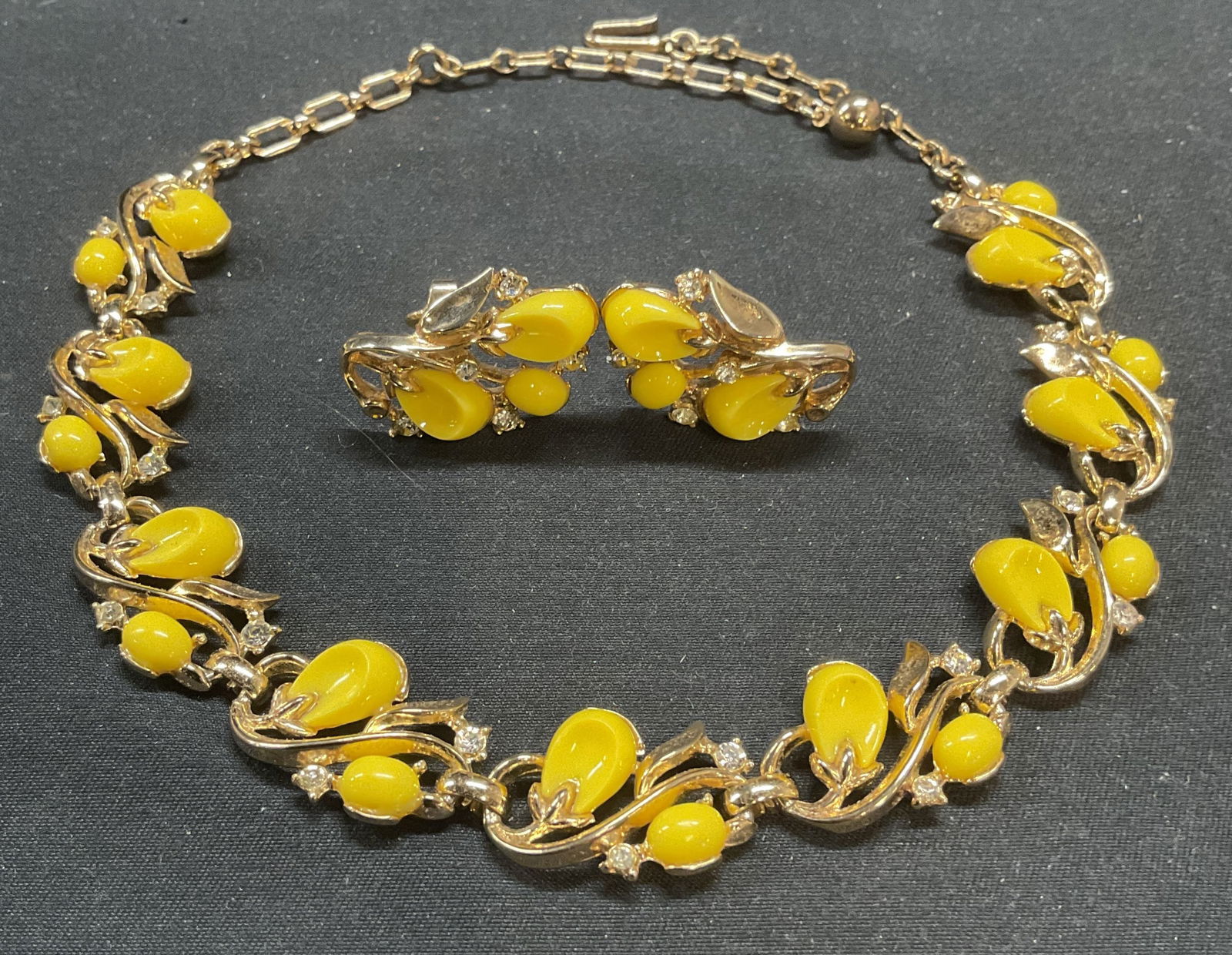 Vintage Trifari Gold Ton Yellow Lucite Jewelry Set: Set of 2 pieces of vintage Trifari jewelry. Gold tone, yellow lucite and colorless crystal choker necklace and clip on earrings with floral design. Signed on earrings. Necklace drop length approx. 5.7