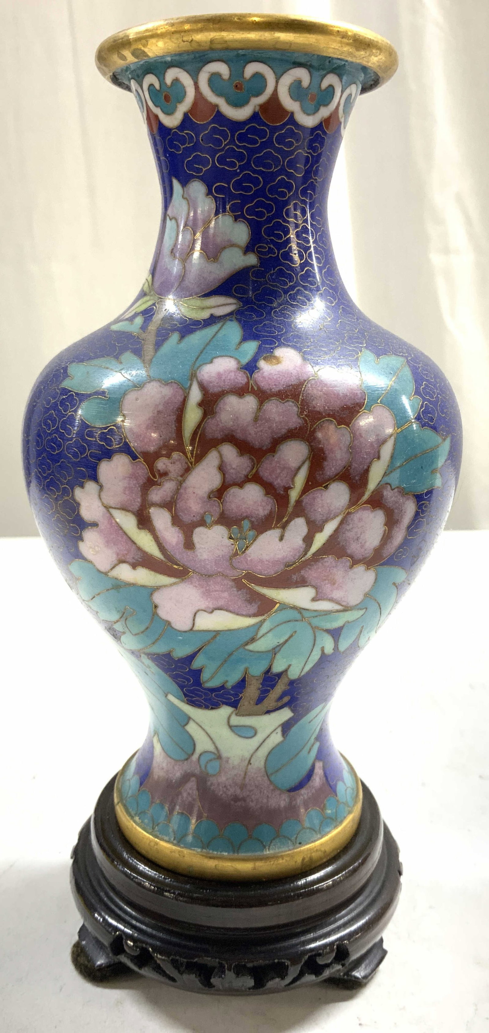 Vintage Asian Cloisonne Vase W Stand: Lot includes 1 vase & 1 mahogany toned stand. Piece is Asian Cloisonne enamel. Vase has multi toned floral and leaf detail. Vase has gilt rim. Stand has pierced detail. Vase on stand measures approx 8