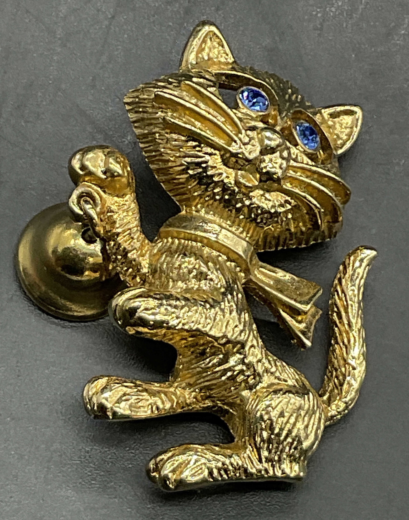 AVON Crystal Eyed Cat W/ Articulated Bell Brooch: A vintage gold tone metal cat form brooch. The cat holds an articulated bell in its paw and has faceted blue crystal eyes. Metal pin closure to reverse. Signed AVON to reverse. Measures approx. 1.5L x
