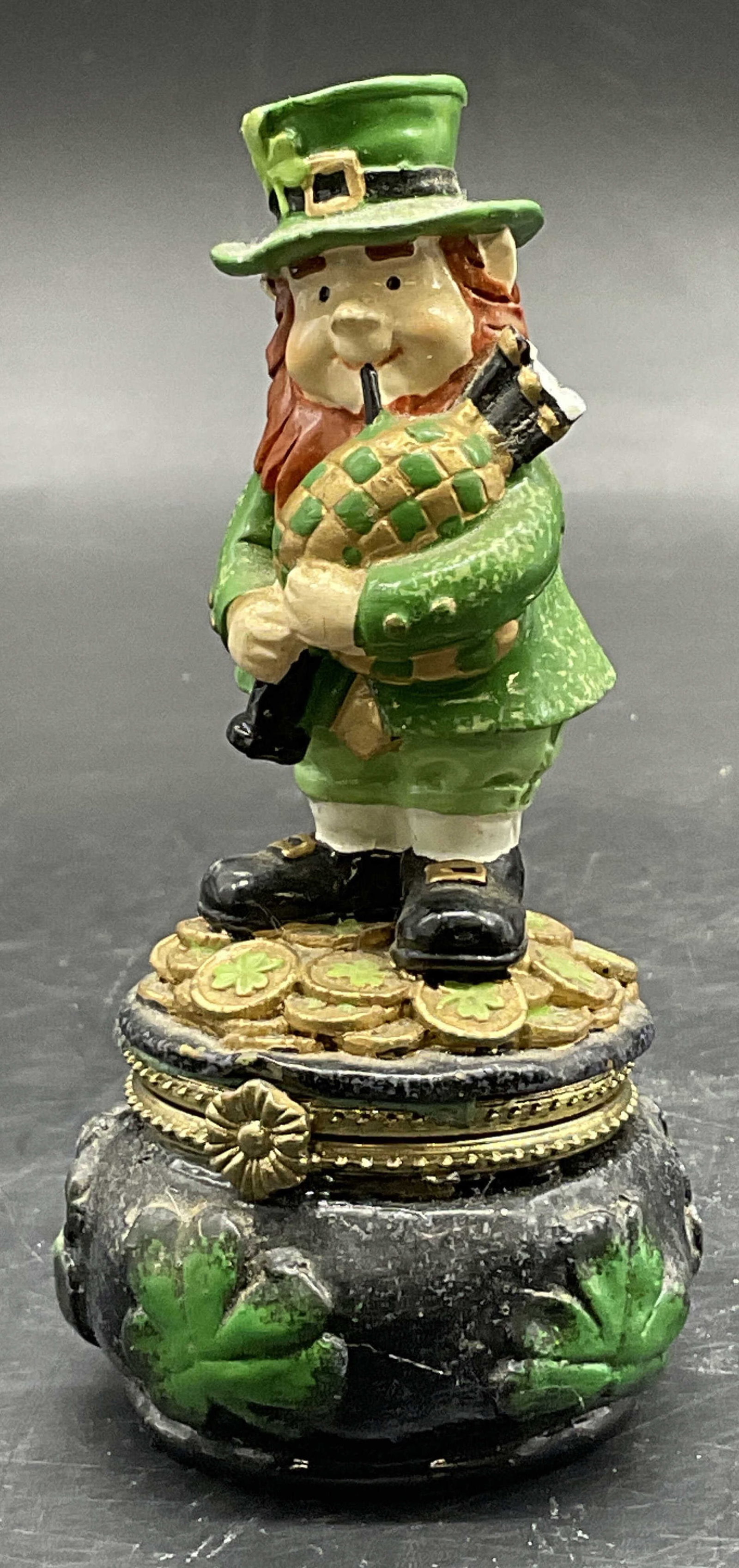 Leprechaun Atop Pot of Gold Figural Trinket Box: Leprechaun Atop Pot of Gold Figural Trinket Box. Crafted from resinous material. Opens with hinge hardware. Measures approx. 4.5H x 1.5W in. Repair present. Residue, discoloration, and surface wear pr