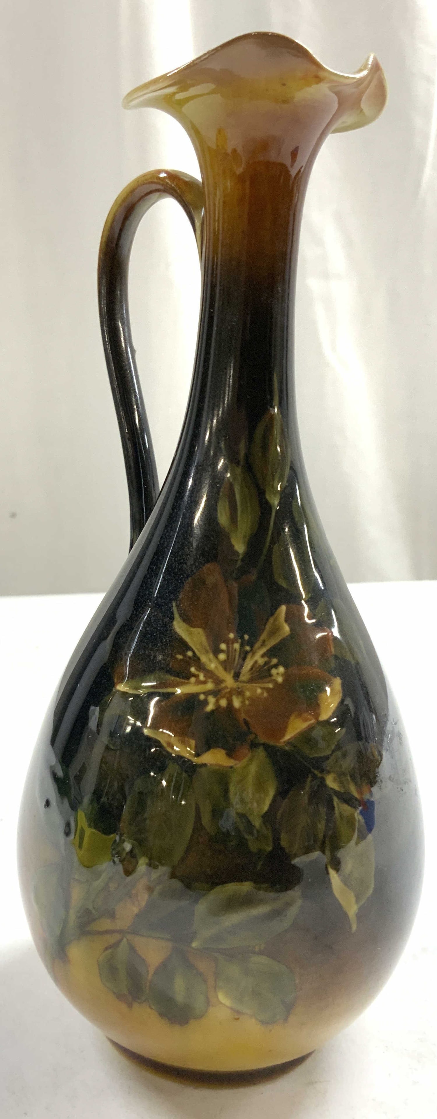 Ceramic Ewer Vase W Floral Detail: Underside appears to be inscribed EDR. Ewer is ceramic. Piece has multi toned floral & leaf detail. Ewer has handkerchief style rim. Piece measures approximately 7 inches tall 3 inches deep & wide. Pi