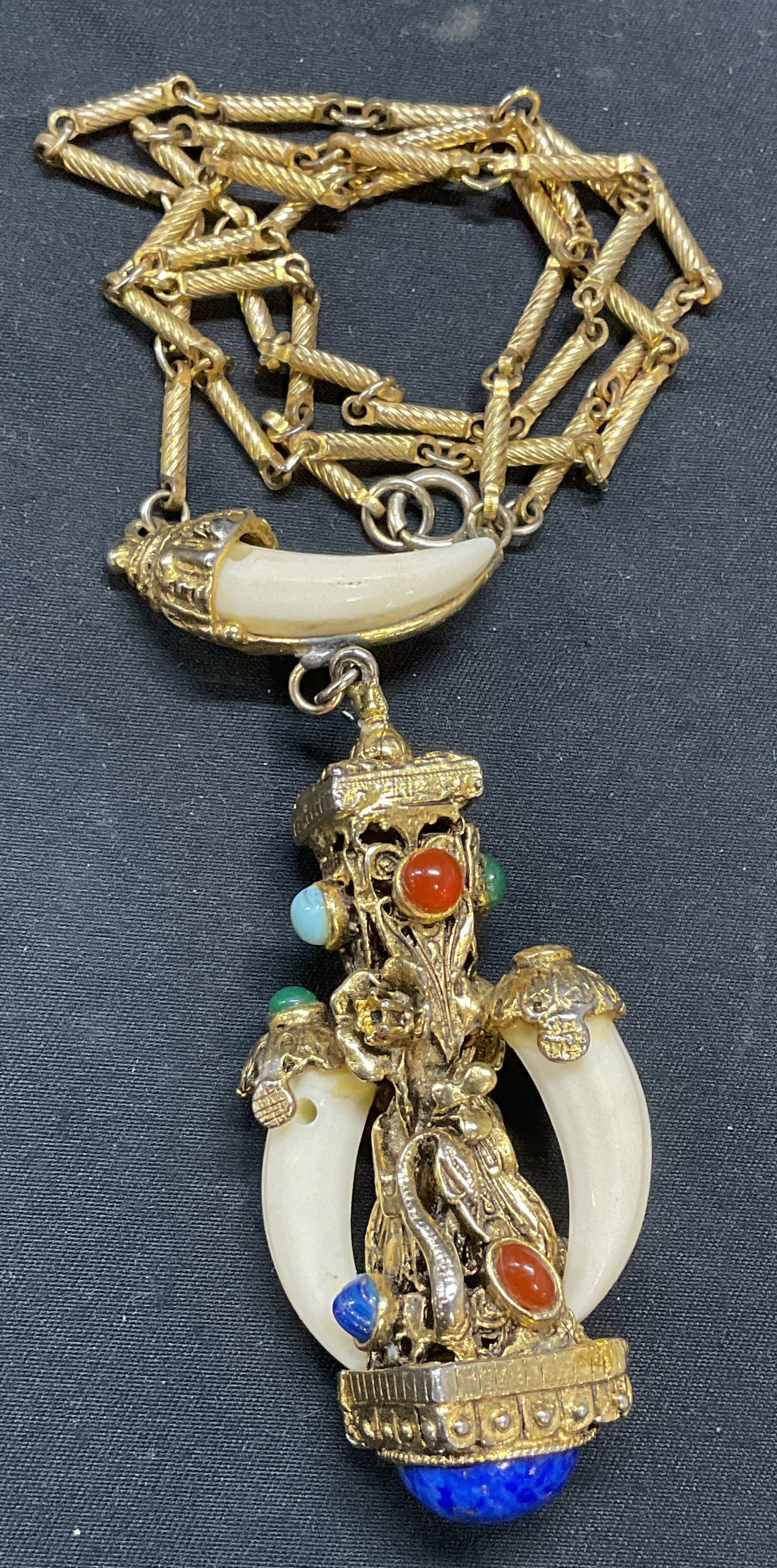 Vtg Kenneth Lane Style Amulet Charm Necklace: A vintage gold tone Etruscan style amulet pendant necklace. Faux gemstone cabochons and faux resin tusk decoration. In the style of Kenneth Lane, no signature observed. Drop length approx. 12 inches. 