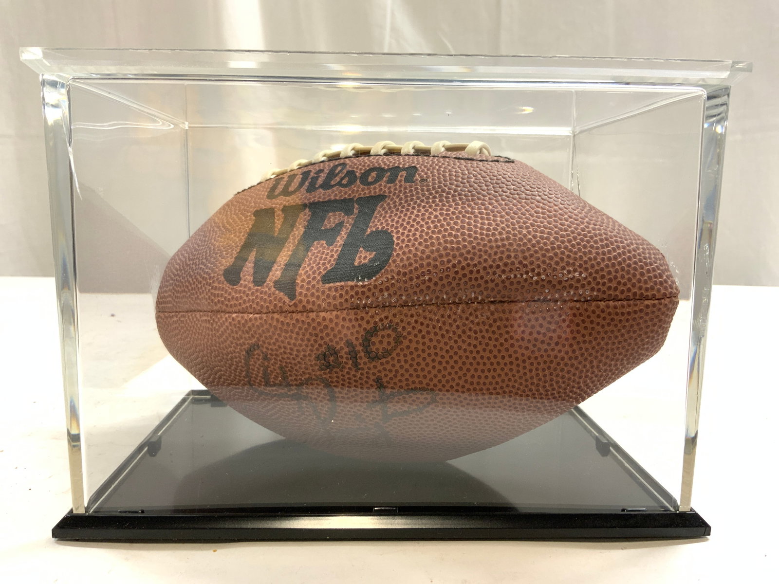 WILSON NFL Signed Mini Football In Case: Football trademarked WILSON NFL. Piece is signed in multiple areas illegibly. Football is in acrylic case with black toned base. Case measures approximately 8 inches wide 5.75 inches tall and deep. Fo