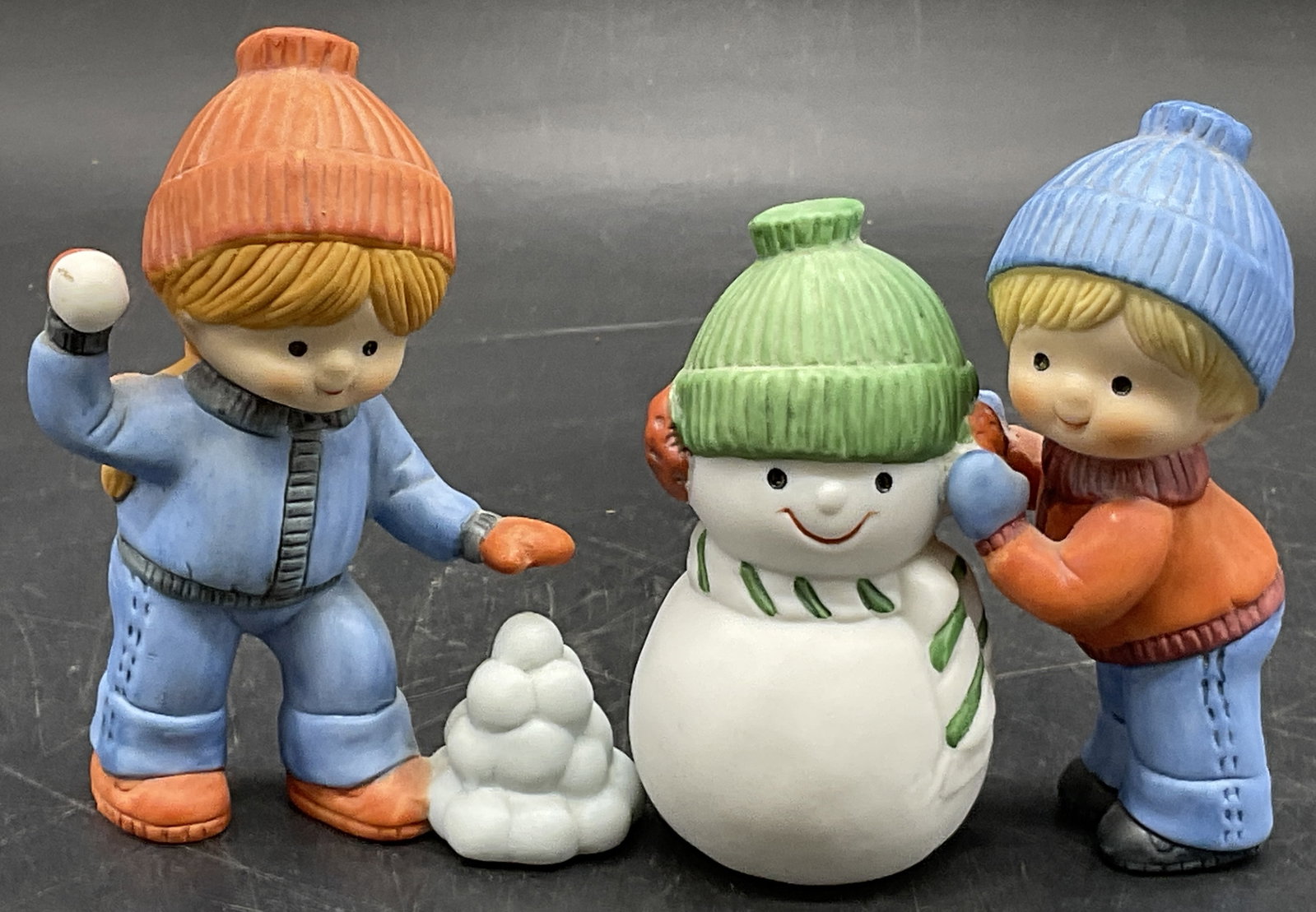 2 ENESCO 1984 Vintage Snowman & Children Figurals: Two figurals featuring a wintertime motif. One figural depicts a young girl tossing a snowball and the other depicts a young boy building a snowman. The boy and snowman need reattachment. Girl figural