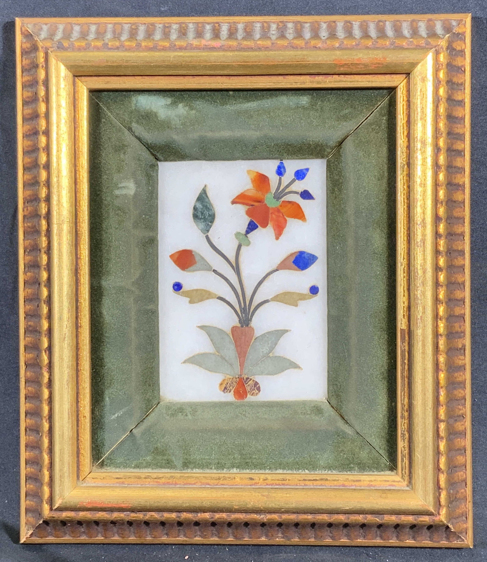 Framed Blooming Flower Stone Inlay Mosaic: Stone inlay mosaic. Subject depicts a flower blooming with multicolored buds and petals. Frames in a wooden gilt frame with lined motifs. Frame measures approx. 7 W x 8 H in. Window measures approx. 2