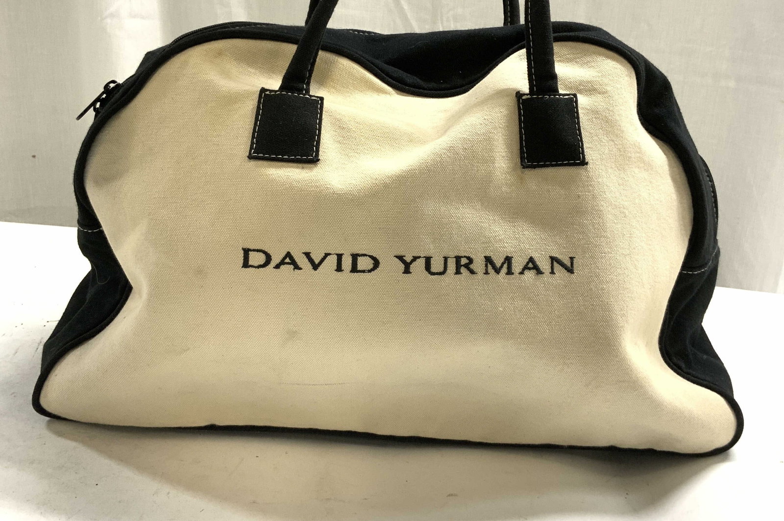 DAVID YURMAN Canvas Tote Bag: Exterior reads DAVID YURMAN. Tote Bag is black and cream toned. Piece has black toned straps. Top of piece is zippered. David YURMAN Canvas tote bag. Piece measures approximately 19.5 inches tall when