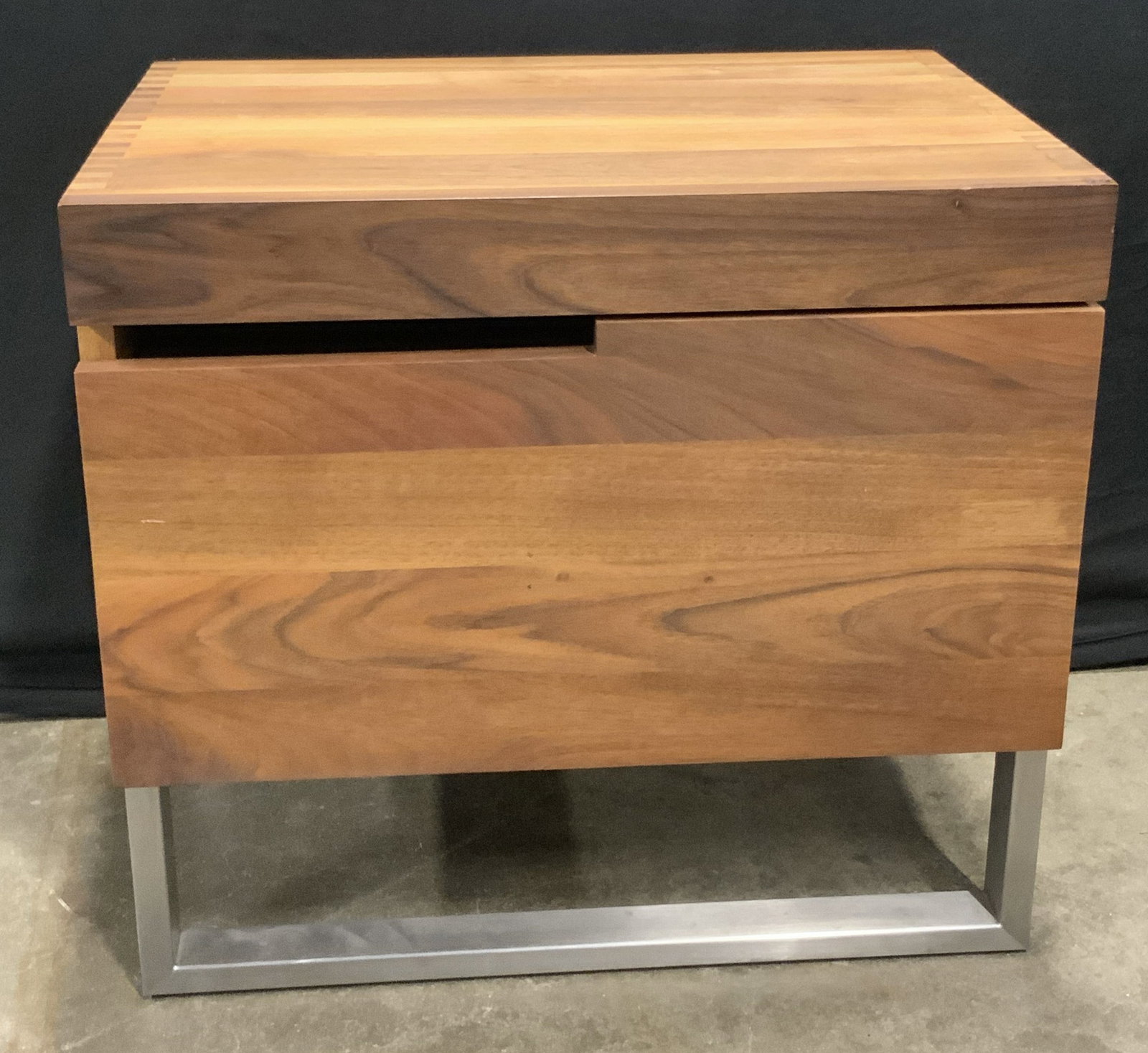 Cube Form Wooden Nightstand W/ Metal Base: A cube form wooden nightstand with a silver tone metal base. One drawer to the obverse. Wood joinery present. Measures approx. 16D x 19.5H x 21.75W in. Some wobble to piece. May need additional hardwa