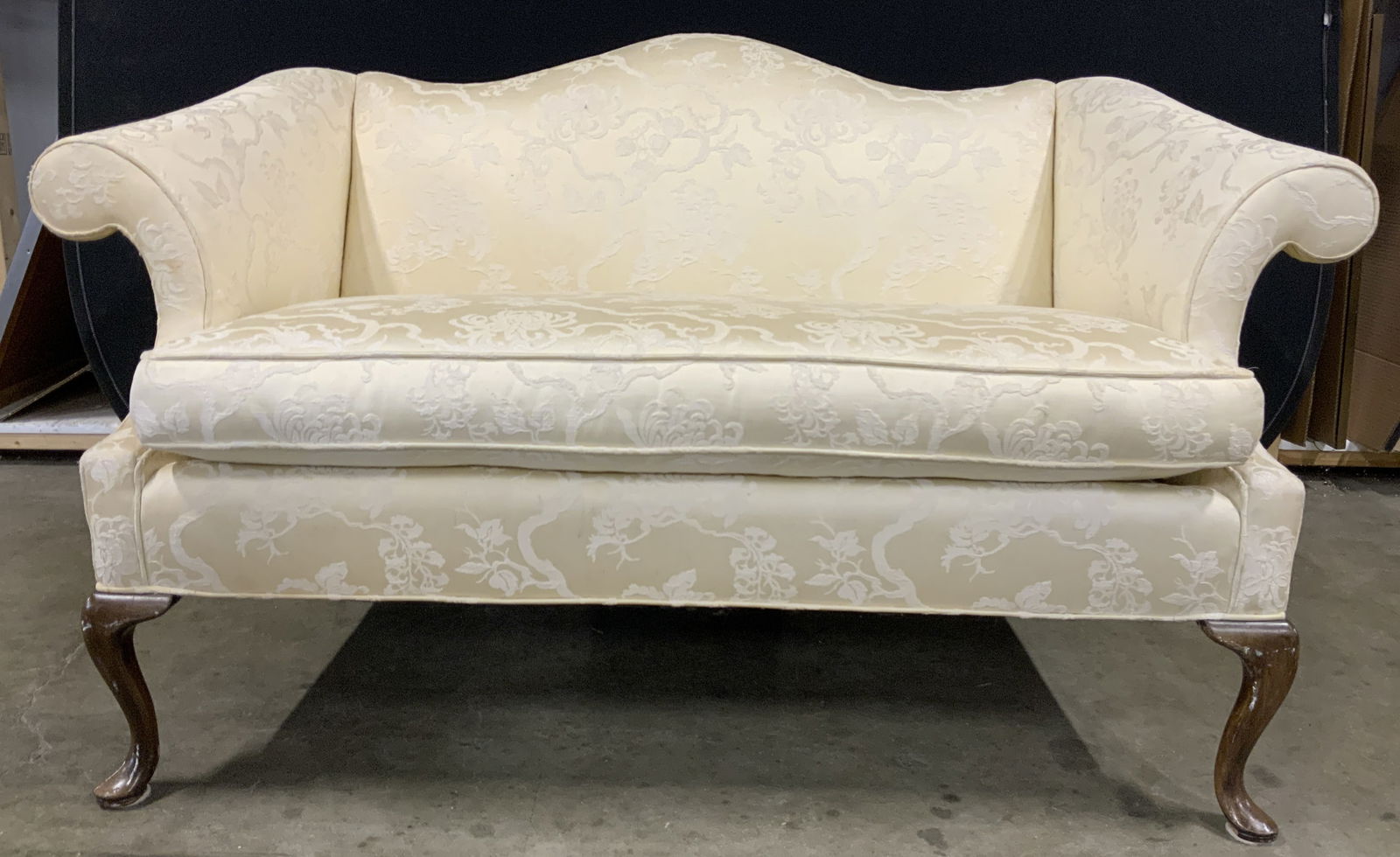 HARDEN FURNITURE Vintage Loveseat: Tag underneath cushion reads HARDEN FURNITURE. Loveseat is upholstered with white gold toned floral and leaf upholstery. Piece has brown toned carved wooden feet. Measures approximately 60 inches long