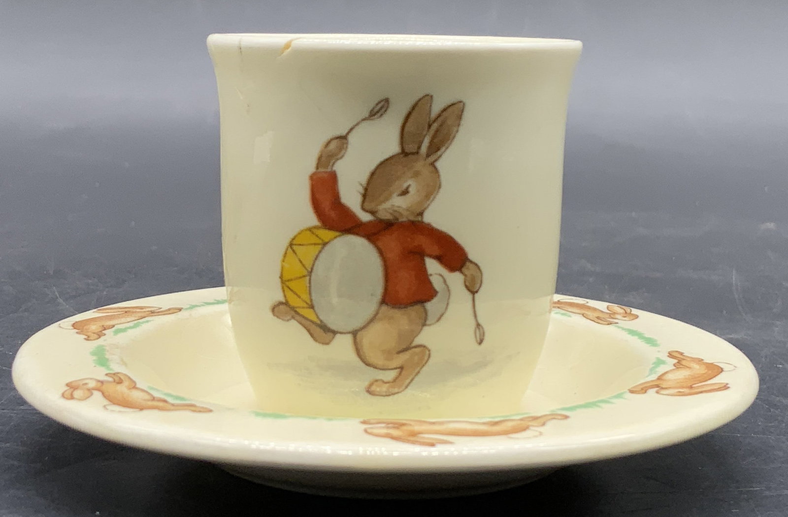 Set2 ROYAL DOULTON BUNNYKINS Cup & Saucer: A set consisting of one vintage cup and one vintage saucer. Undersides are signed ROYAL DOULTON BUNNYKINS. Pieces feature rabbit motifs. Cup measures approx. 2H x 2W in. Cracking and chipping present.